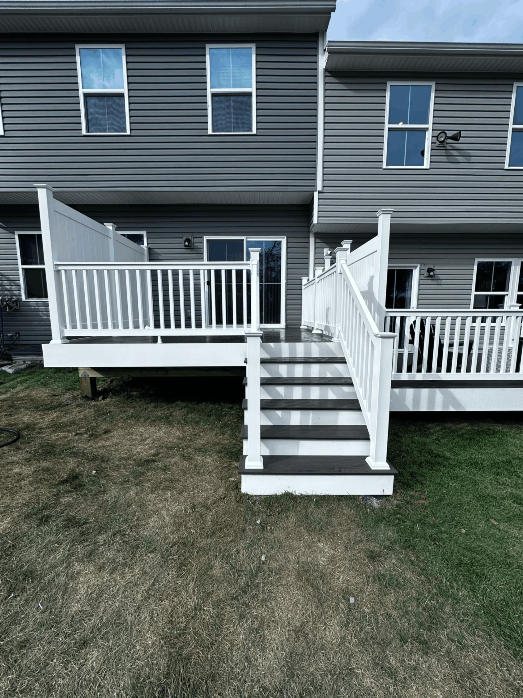 Two-story gray home with a white railed deck and dark stair treads