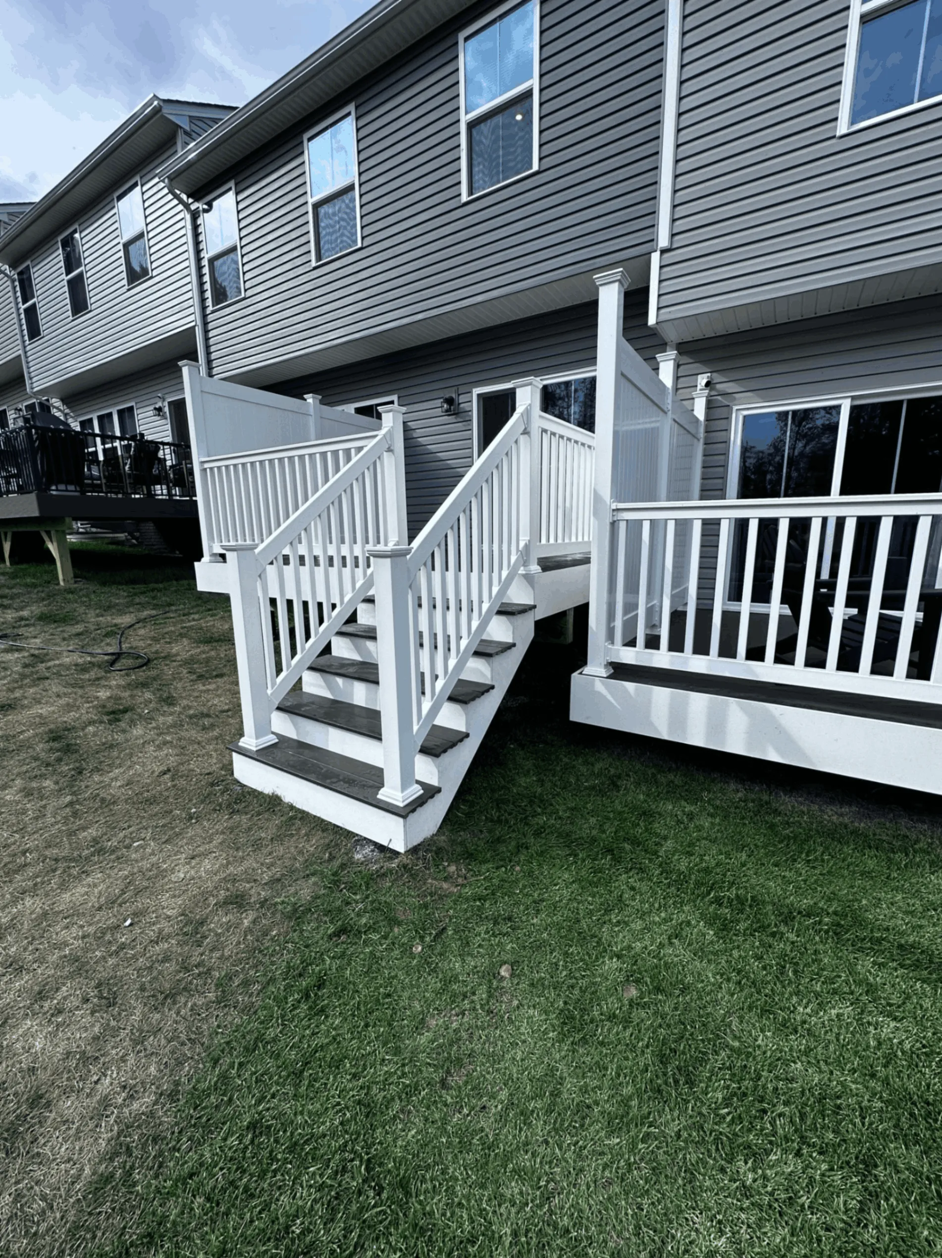 White vinyl deck railings and stairs descending to a lawn behind a gray home