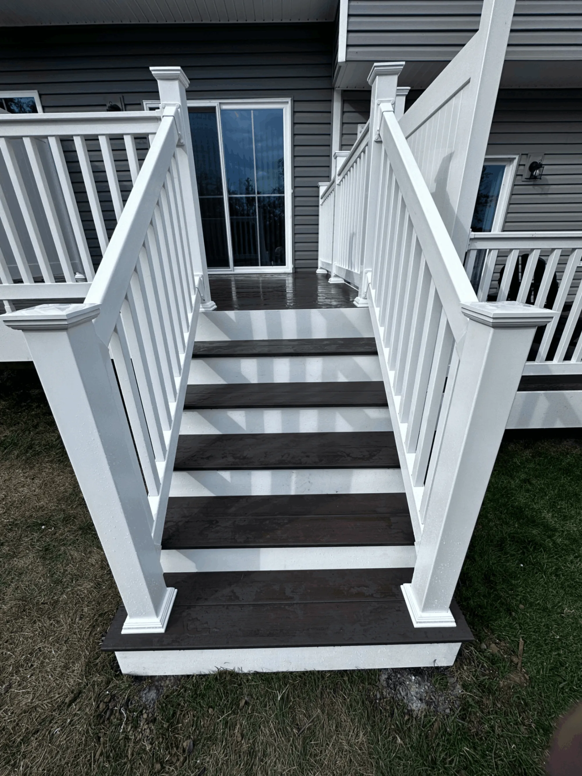 Deck stairs with dark brown treads and white vinyl railings at a rear entry