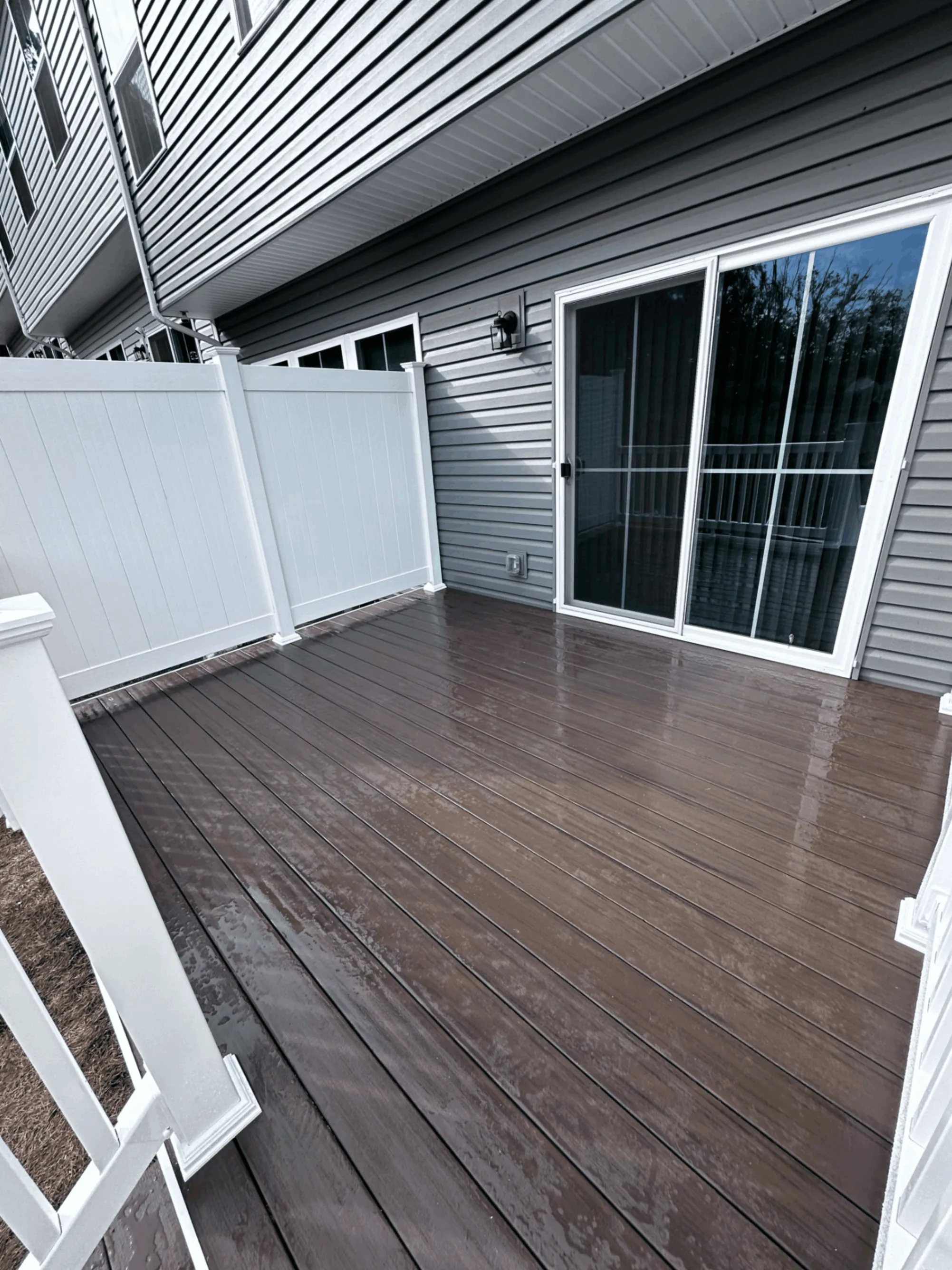 Dark brown composite deck with a white privacy screen beside sliding glass doors