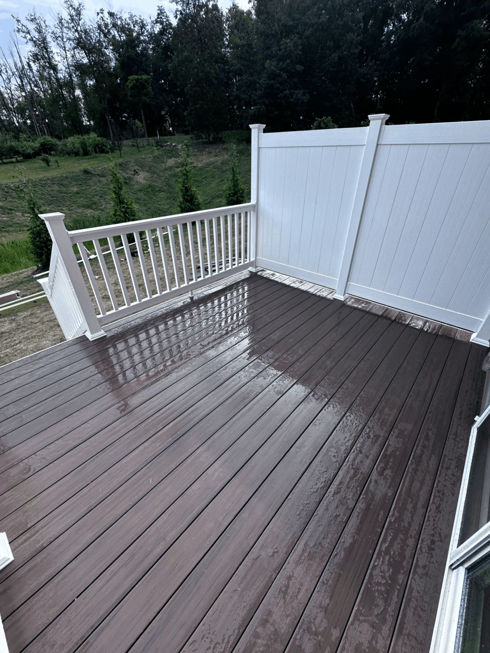 Dark brown composite deck with white vinyl railing and privacy fence panel