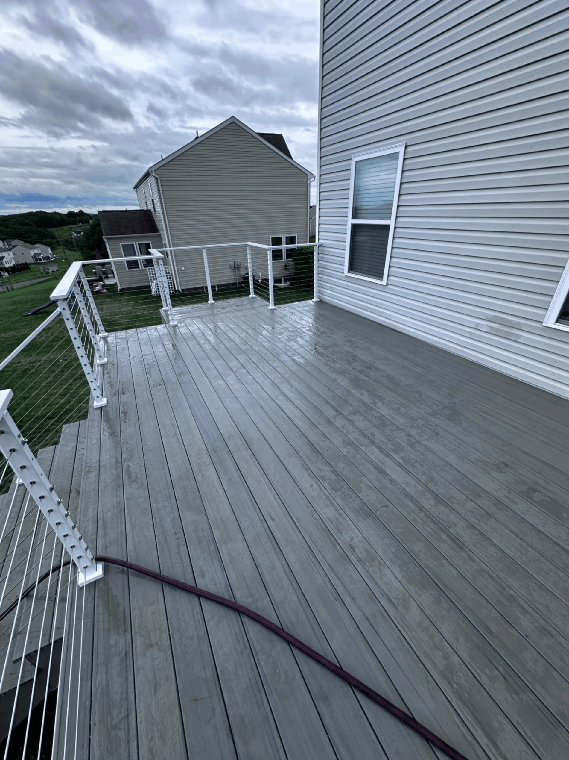 Wet gray composite decking with white cable railing at the corner of a home