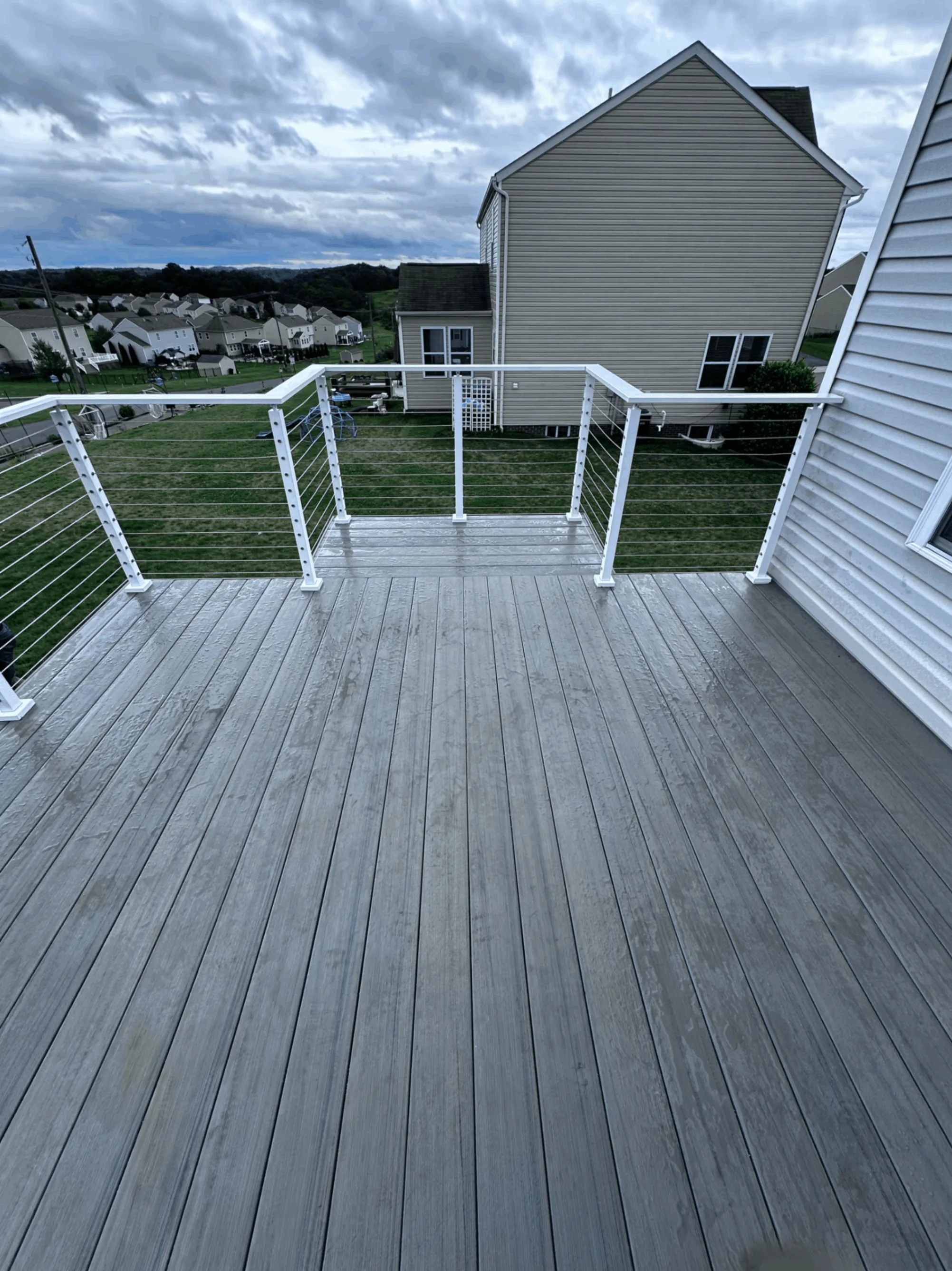 Gray composite deck with white cable railing overlooking an open lawn