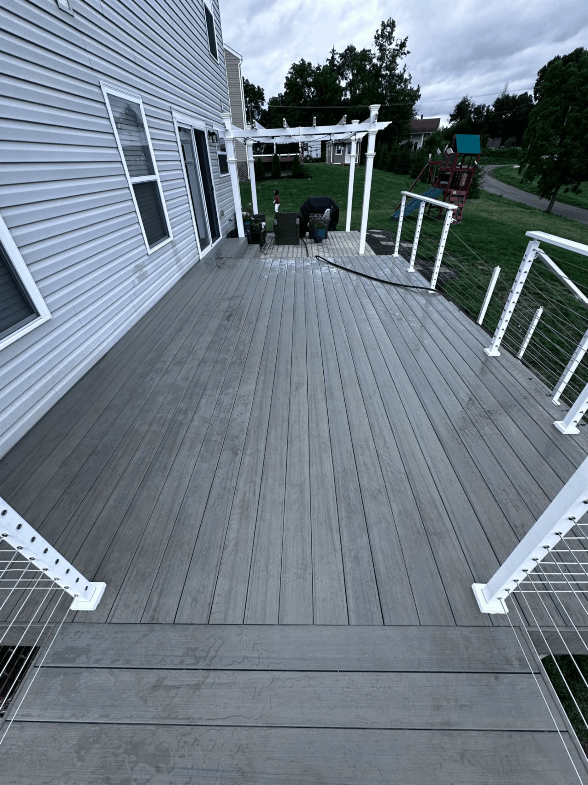 Gray composite deck with cable railing leading toward a backyard pergola