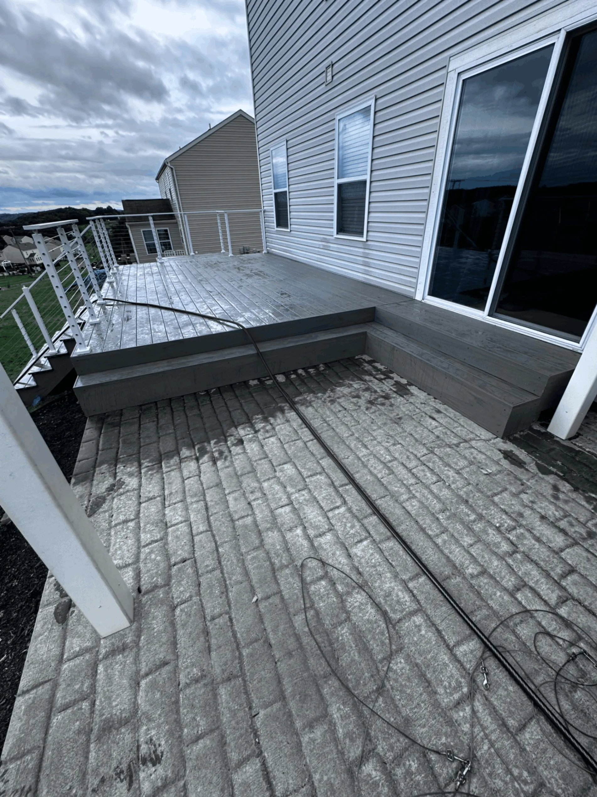 Gray composite deck with white posts and cable railing above a stamped concrete patio