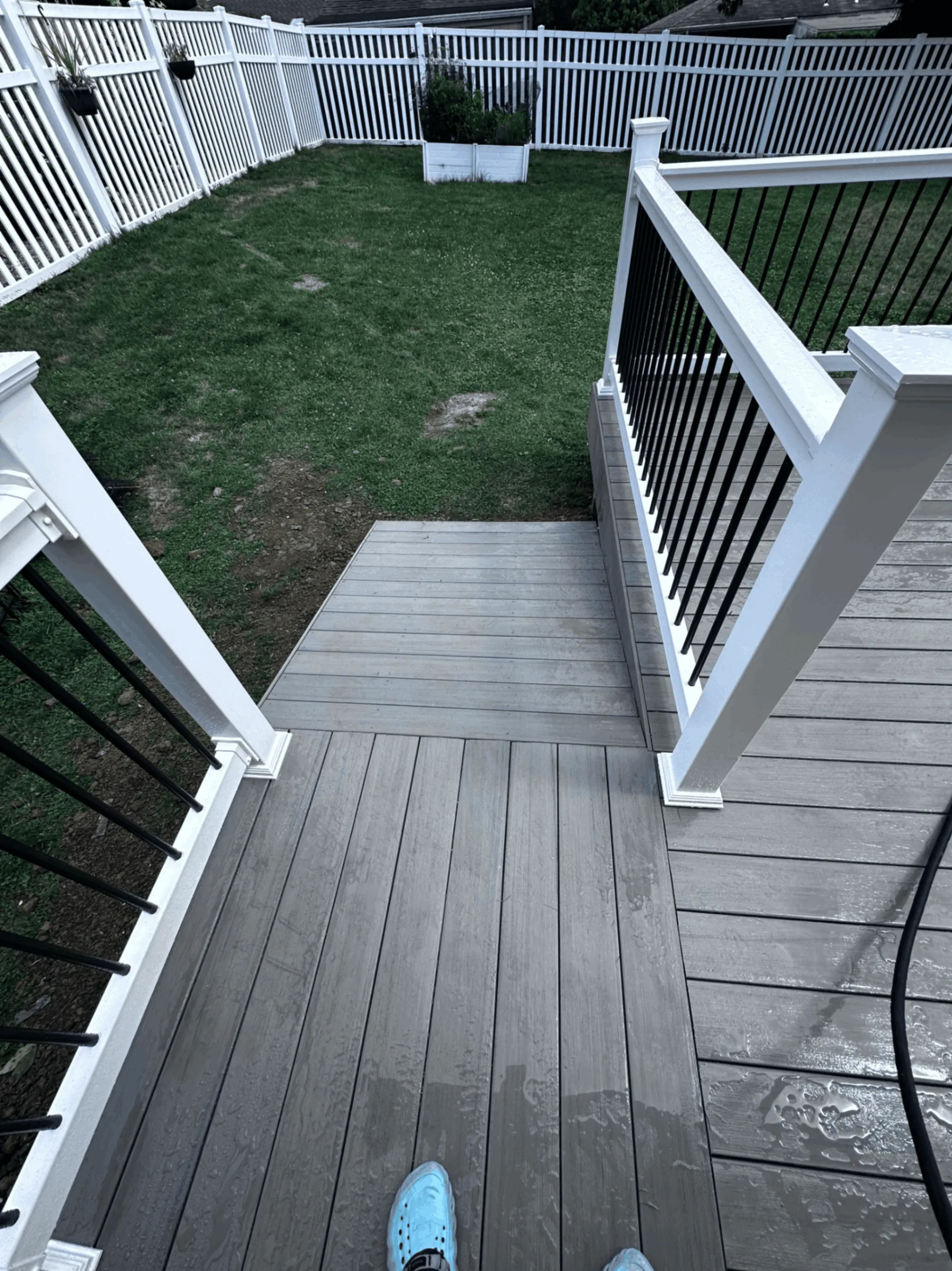 Gray composite deck landing with white posts and black balusters above a lawn