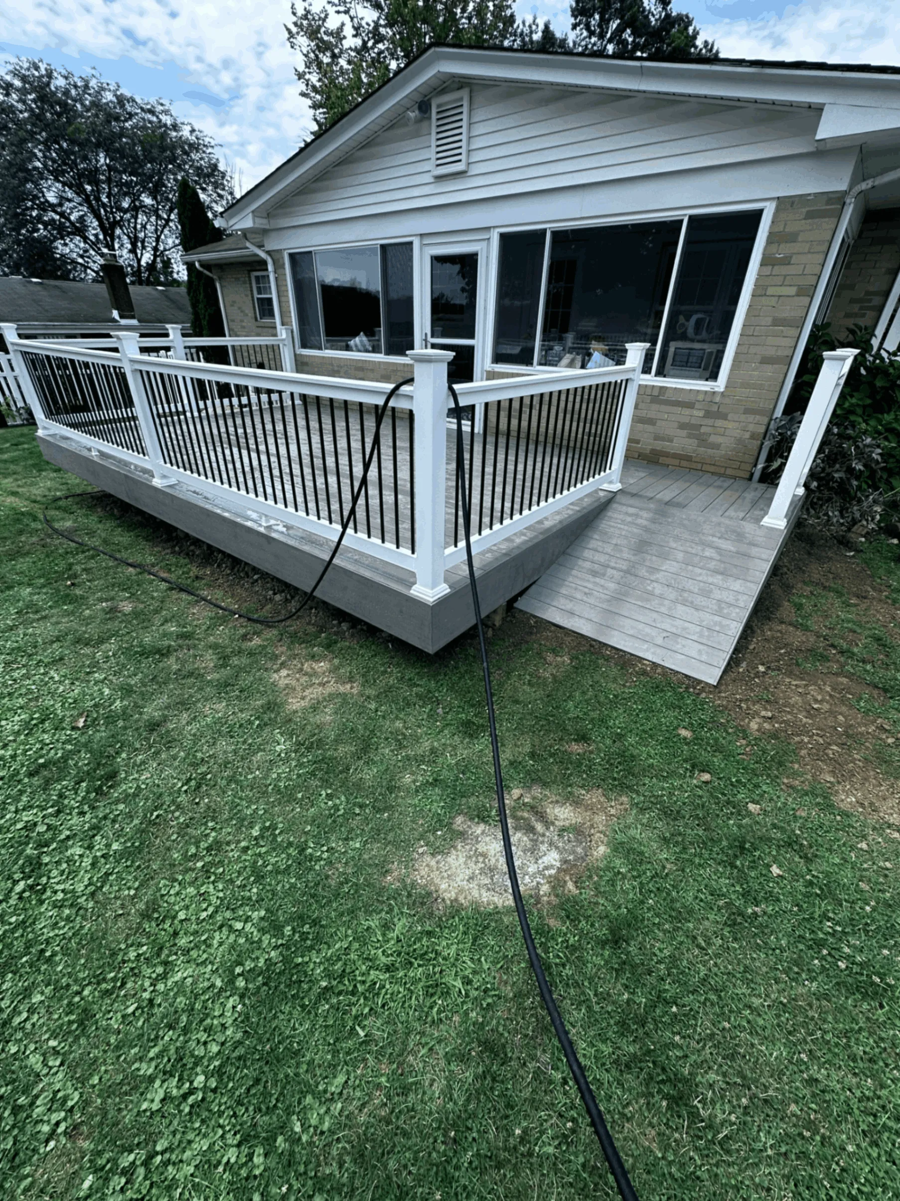 Gray deck with white railings adjoining a sunroom and concrete patio