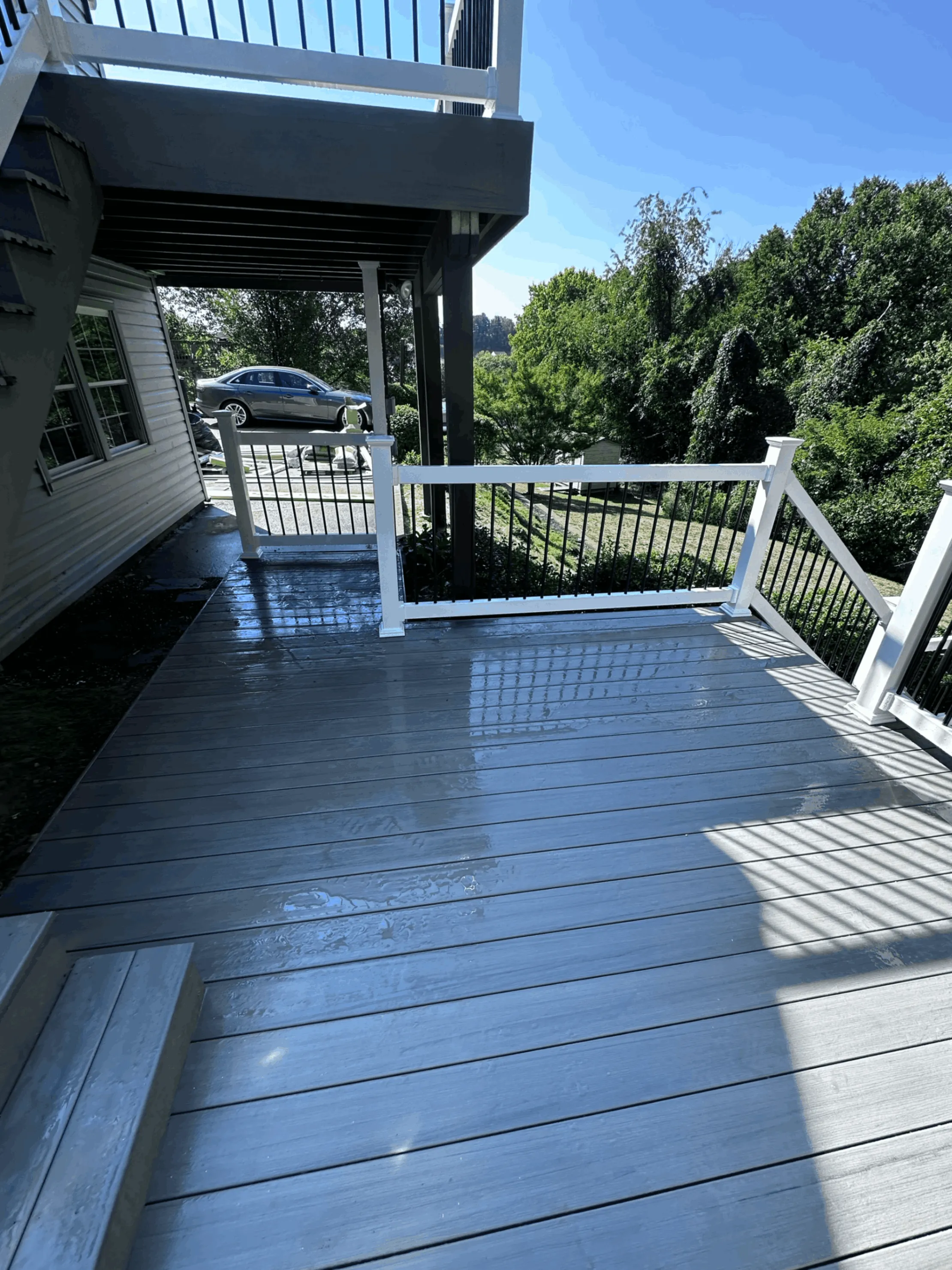 Covered gray composite deck with white railings beside a white sided home