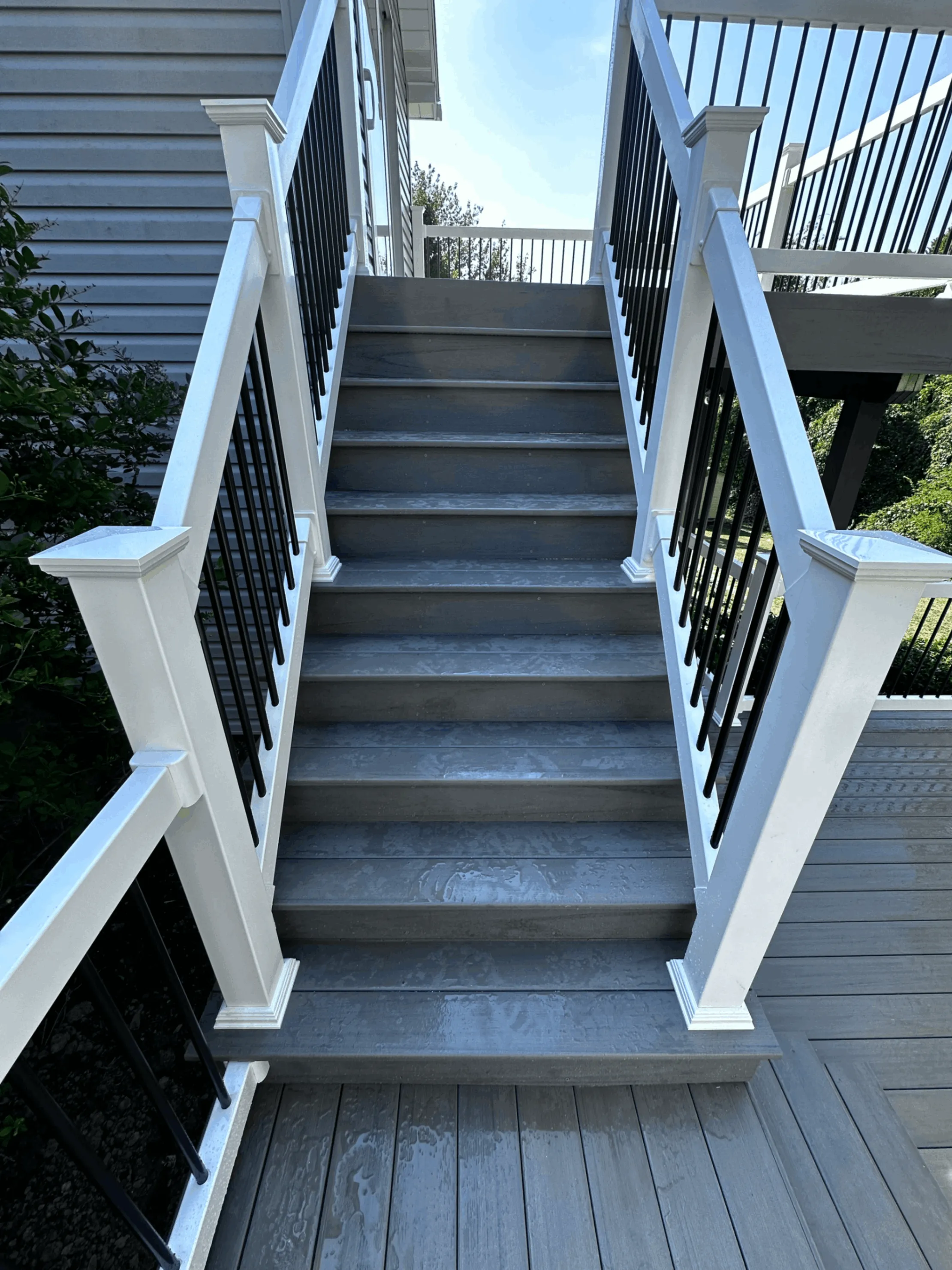 Gray deck stairs rising between white posts with black aluminum balusters
