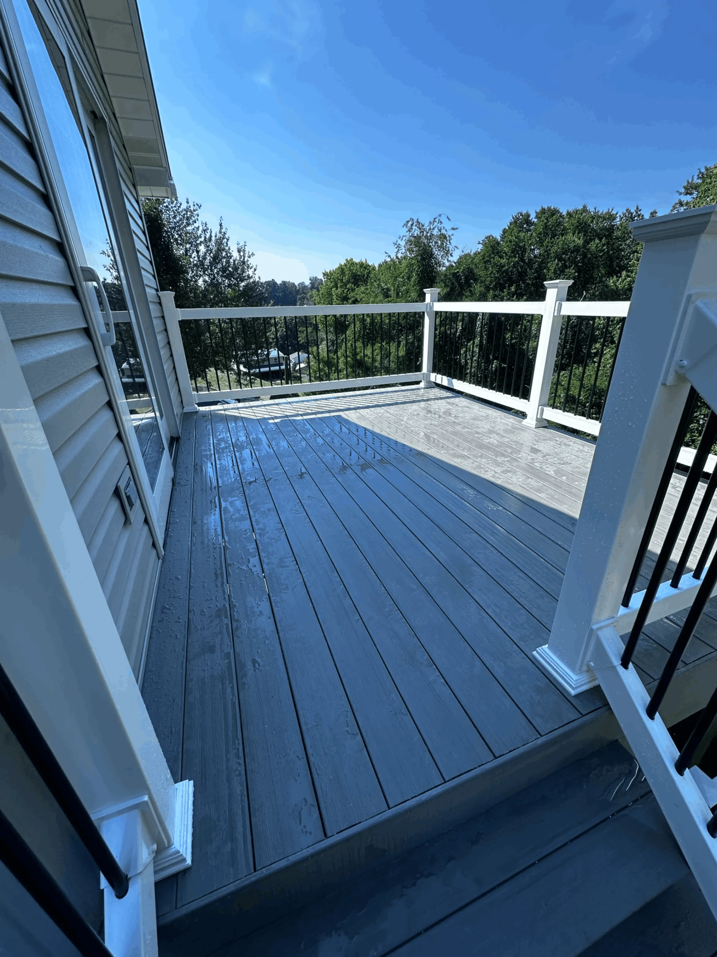 Wet gray composite decking with white railings overlooking a valley