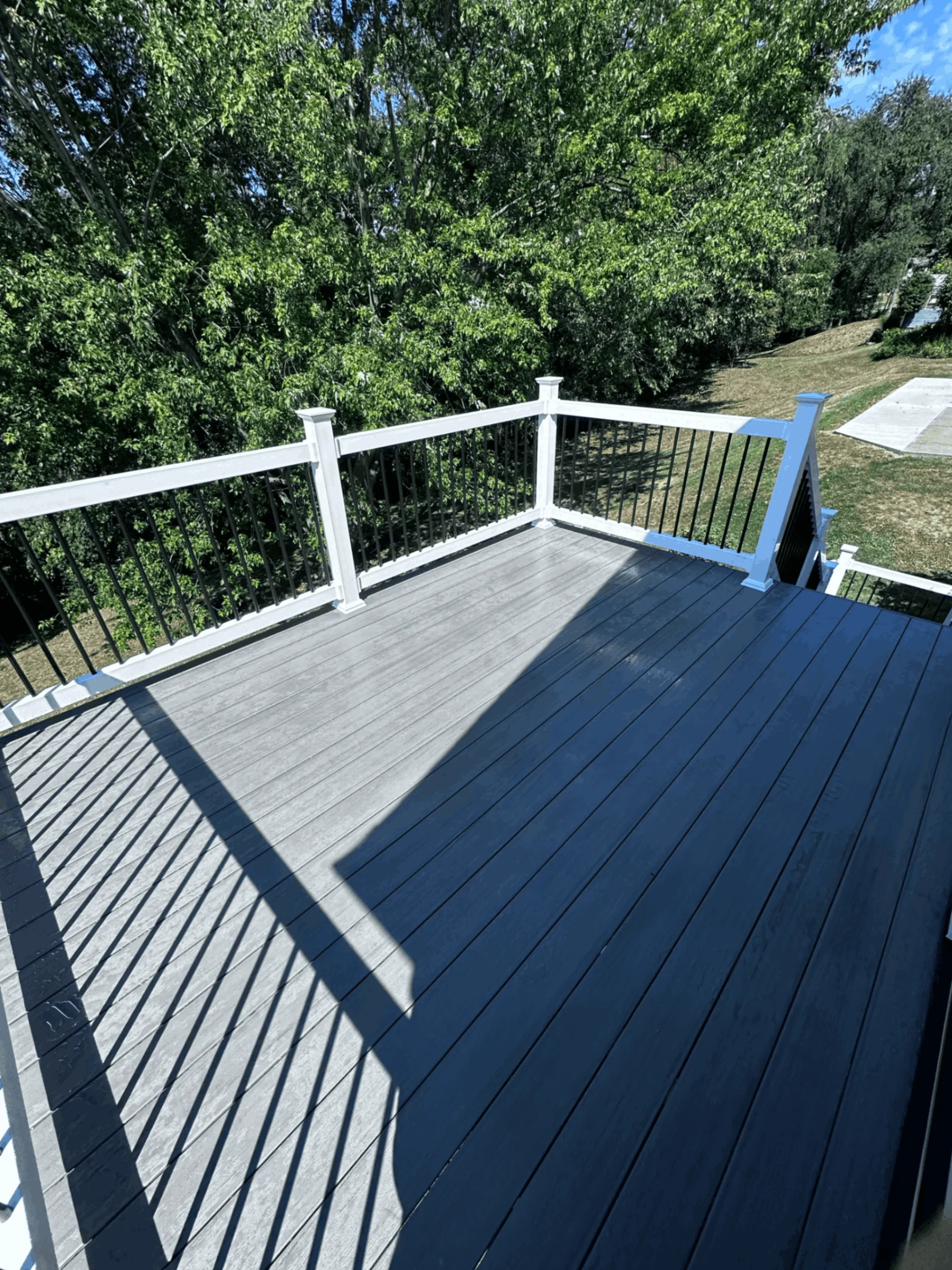 Gray composite deck with white railings and black balusters framed by trees