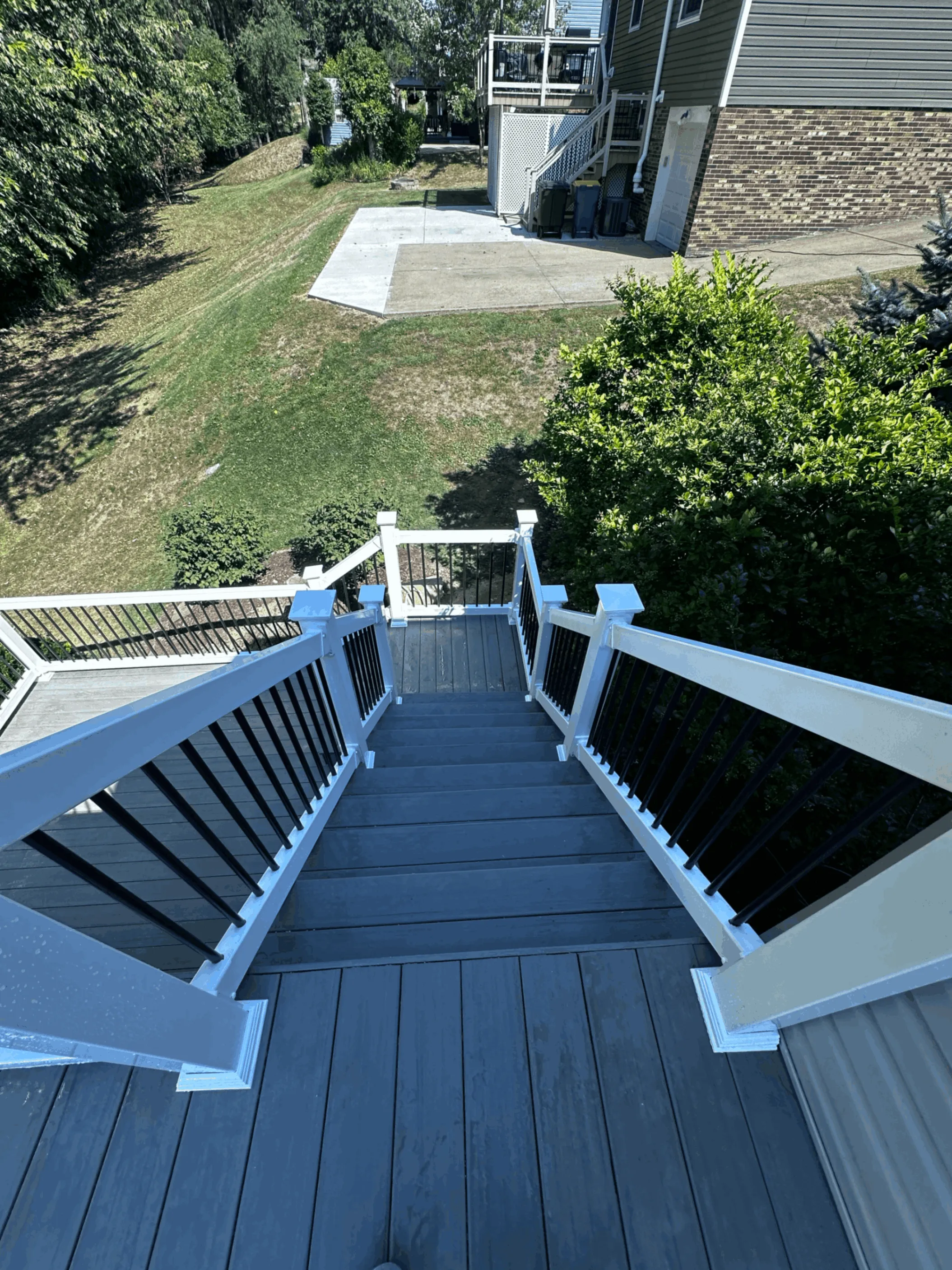 Gray composite deck with white posts and black balusters above a sloped yard