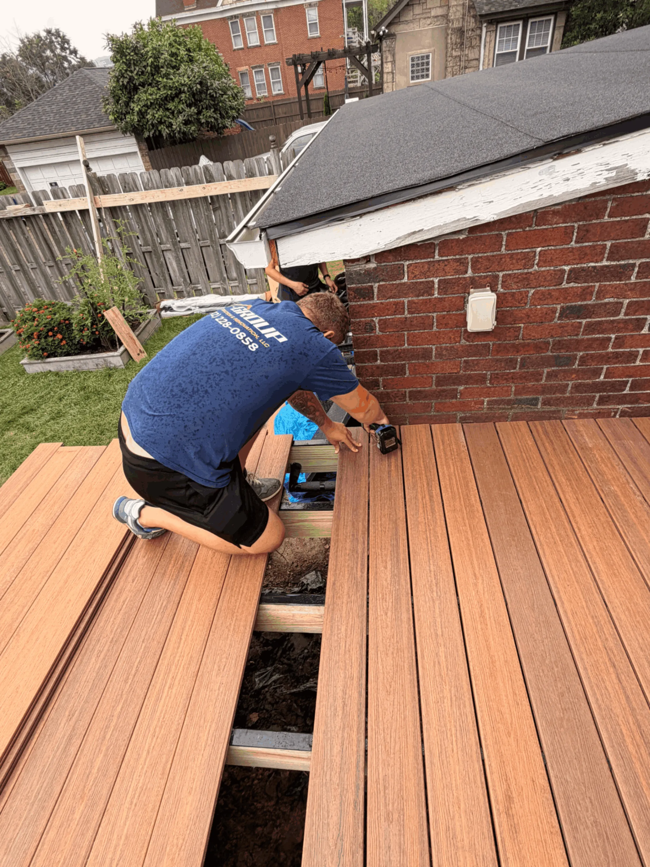 Installer fastening brown composite deck boards beside a brick home