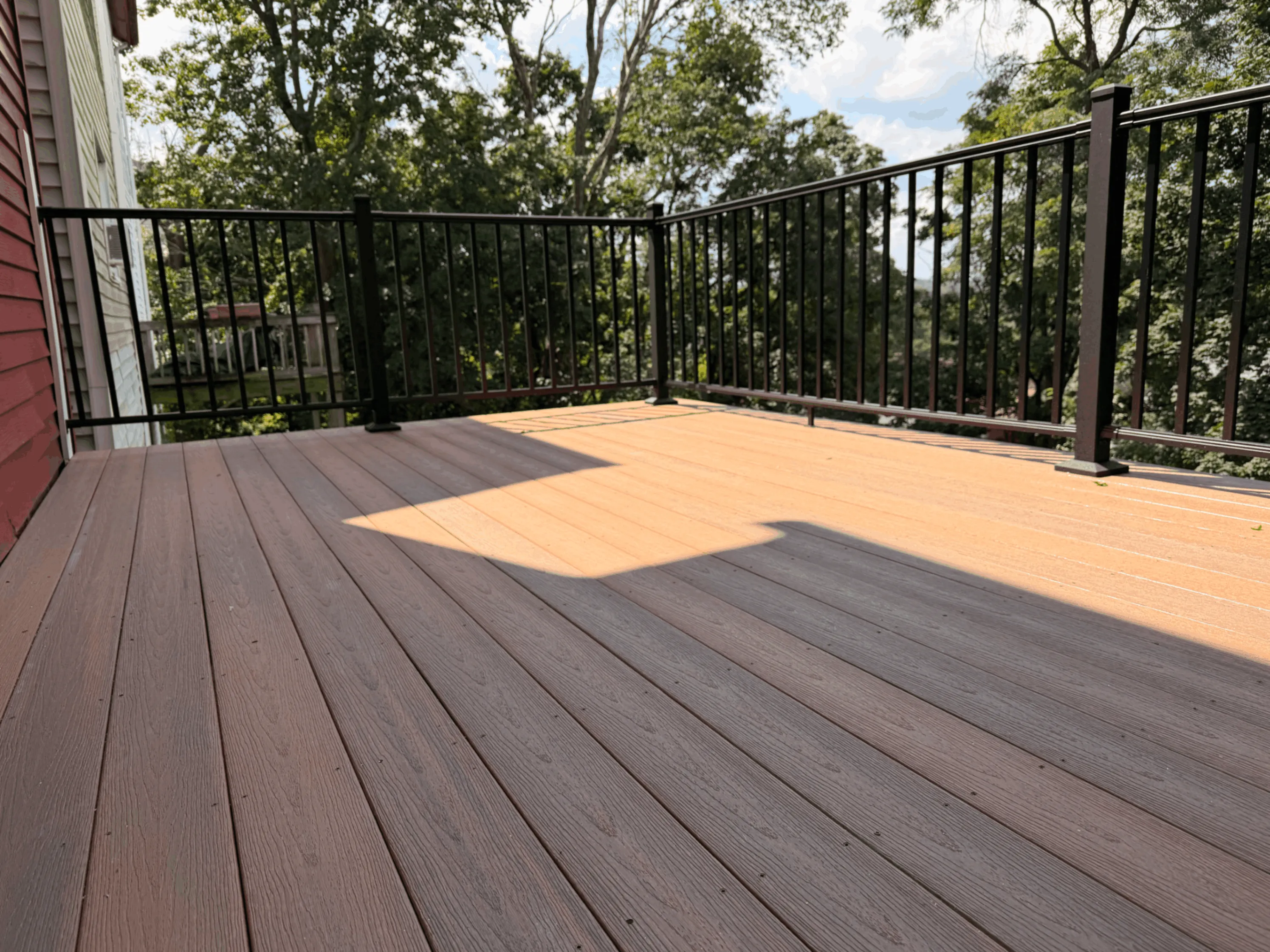 Brown composite deck with black aluminum railings and a hillside treetop view