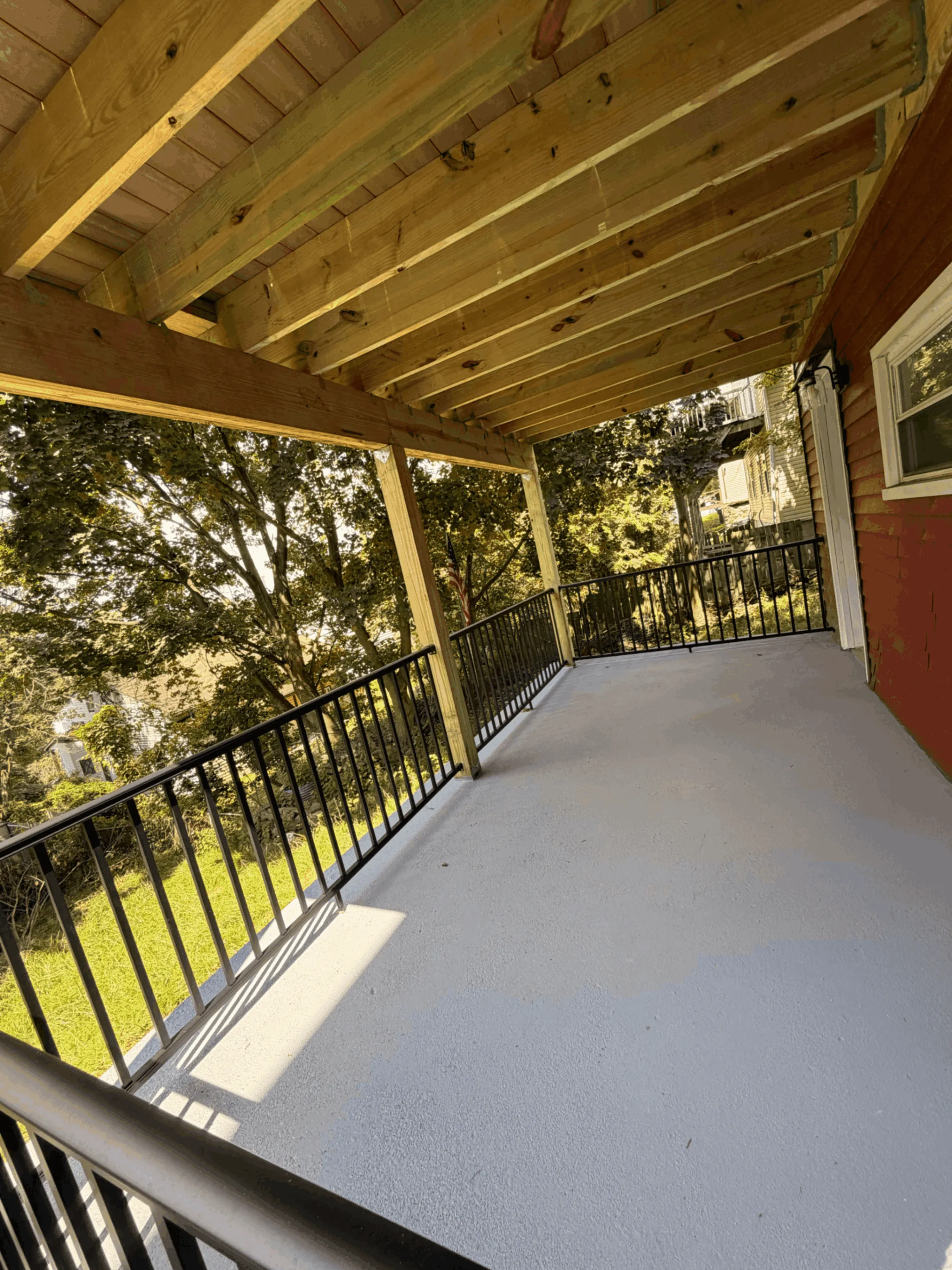 Covered deck with an exposed wood ceiling, black railings, and gray decking