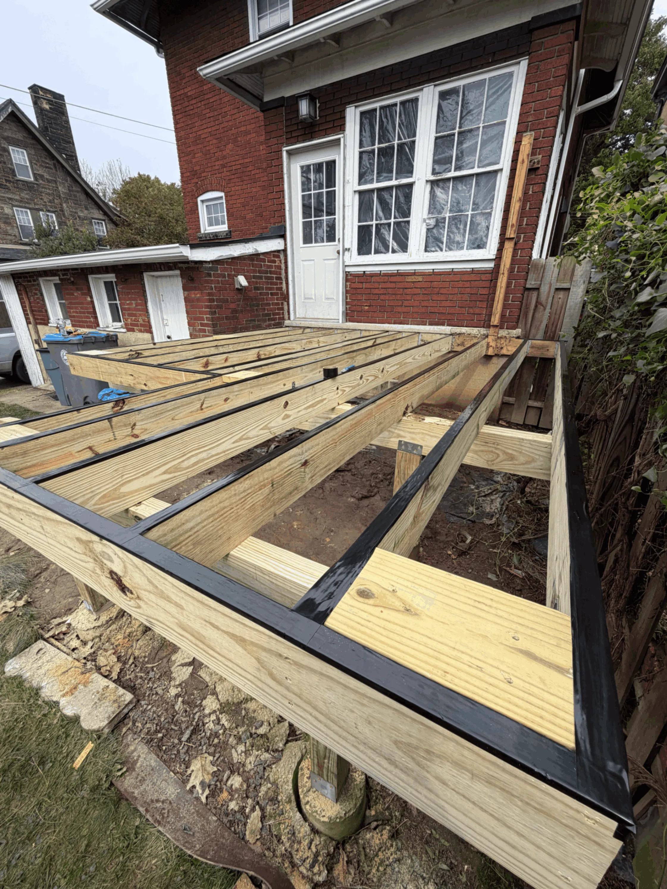 Pressure-treated deck framing and joists installed against a brick home