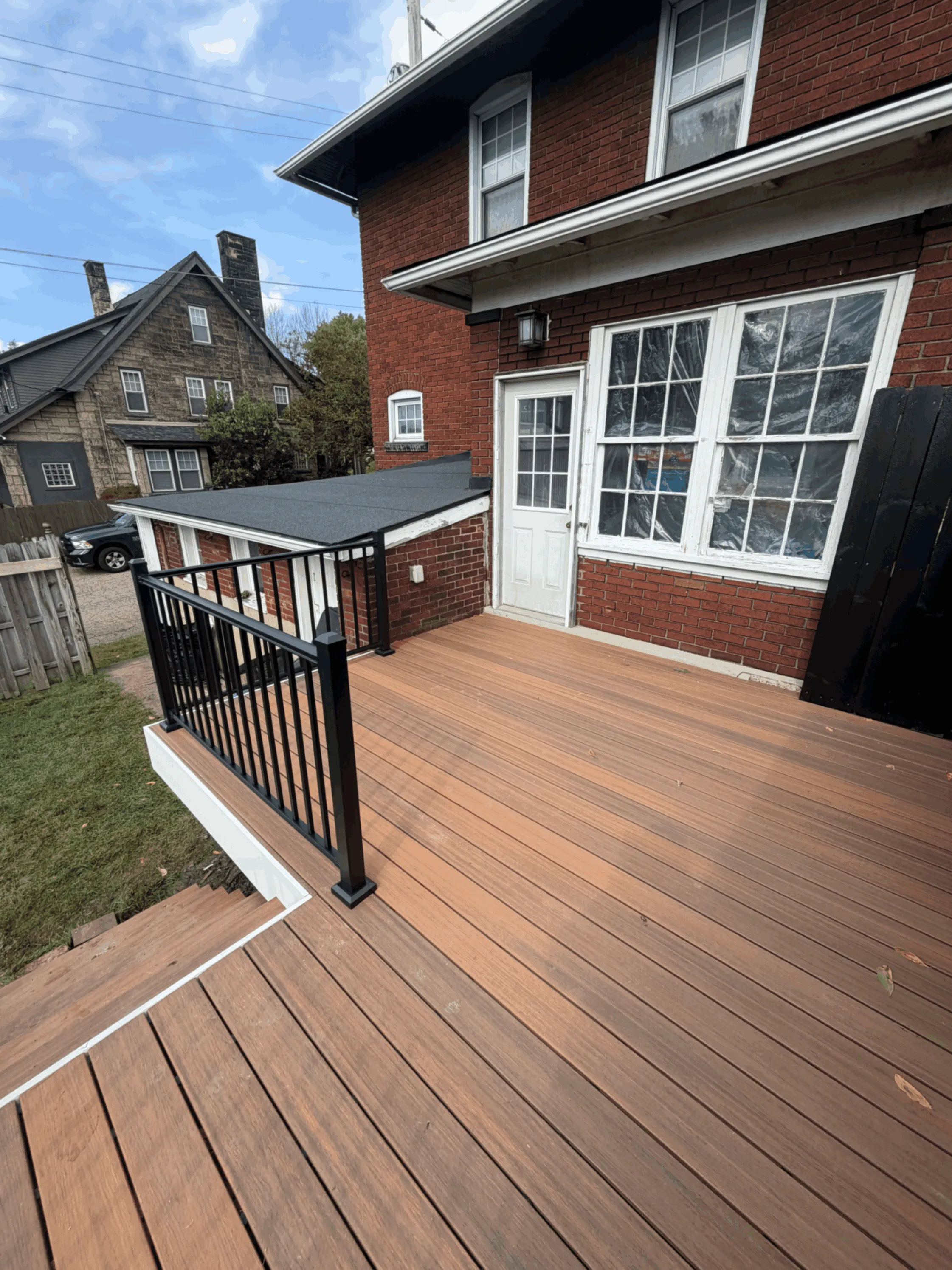Multi-tone composite deck with black aluminum railings behind a red brick home