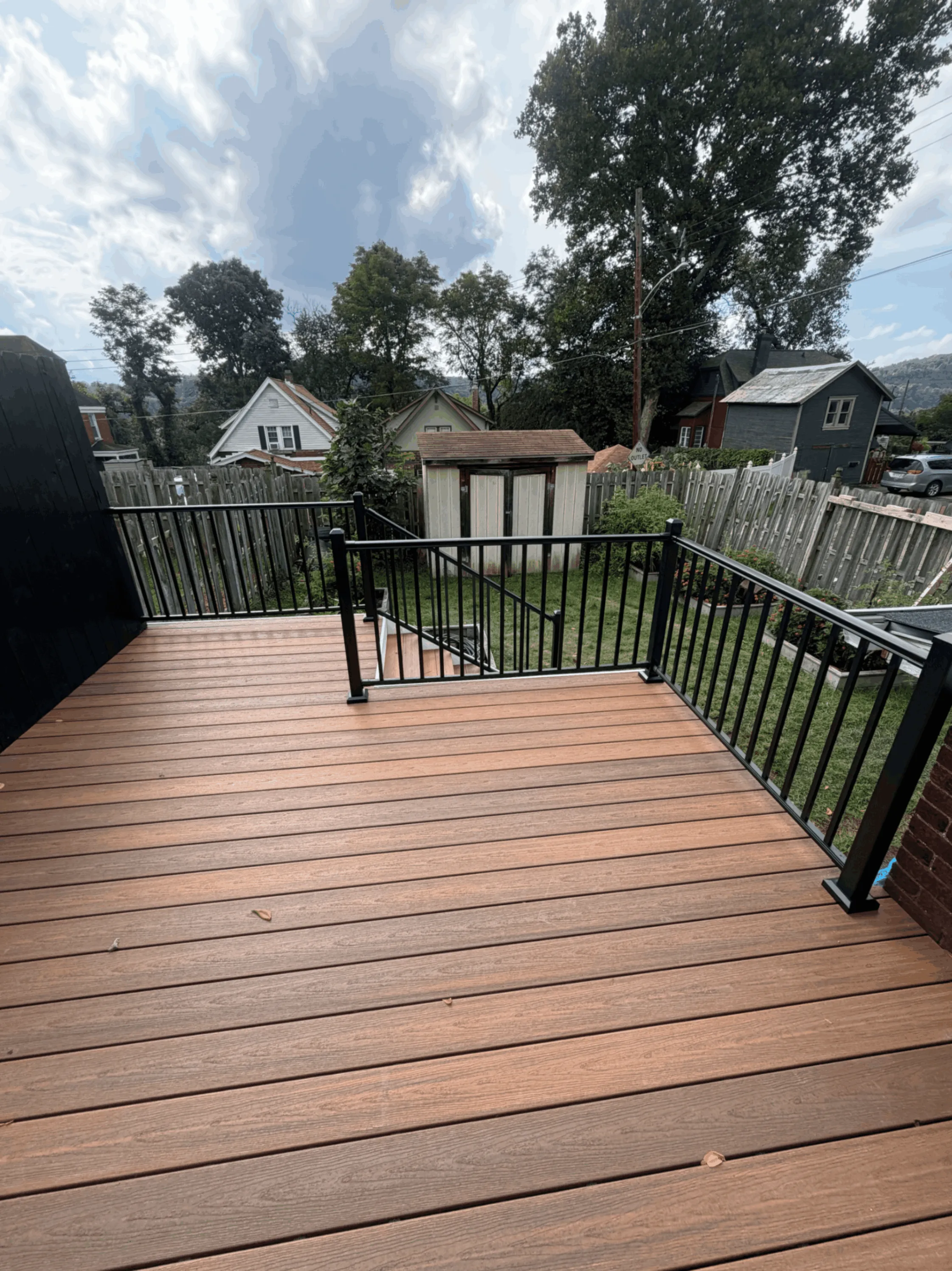 Reddish-brown composite deck with black aluminum railings and a backyard shed