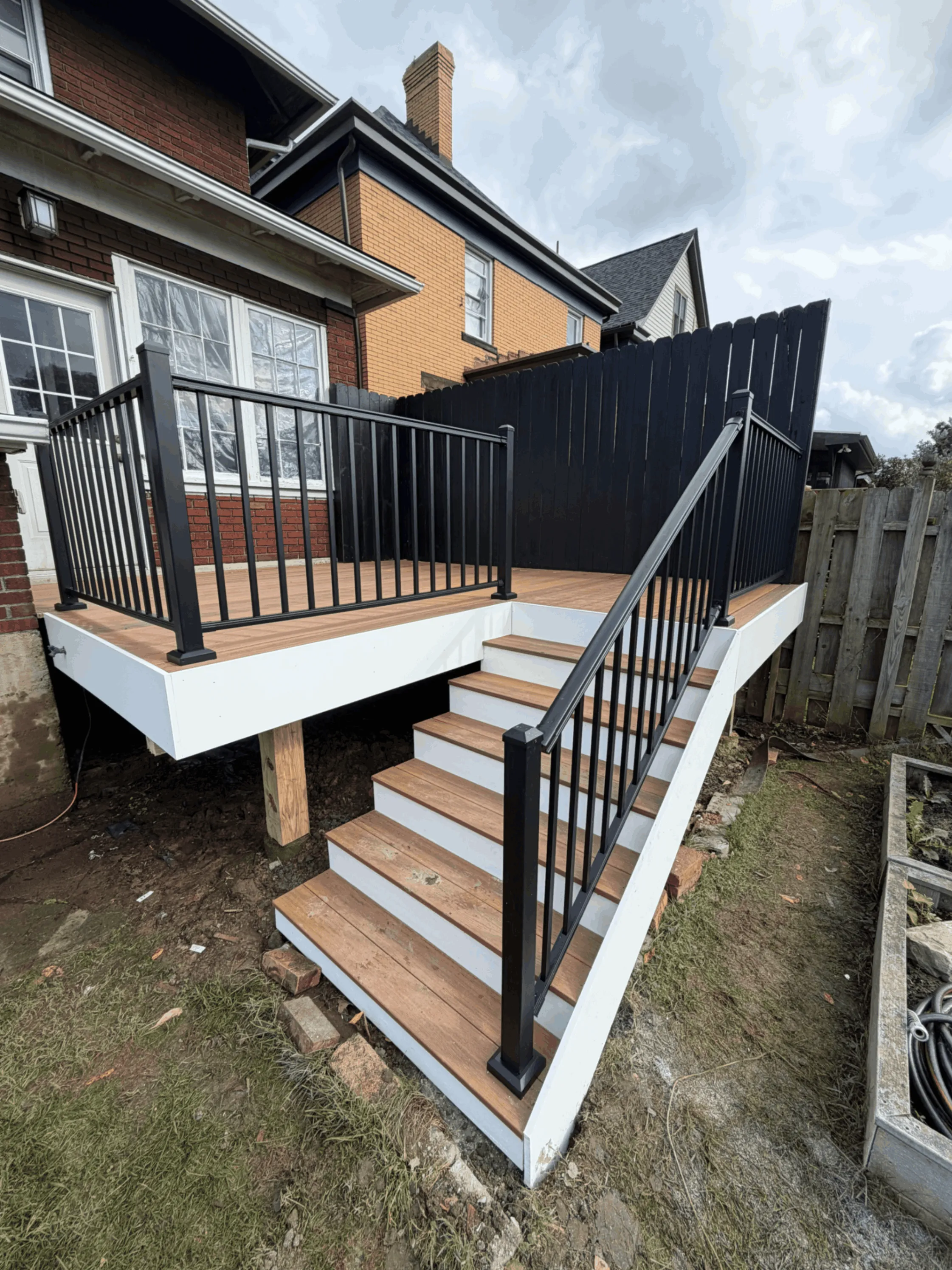 Deck on a brick home with black railings, a privacy screen panel, and tan stair treads