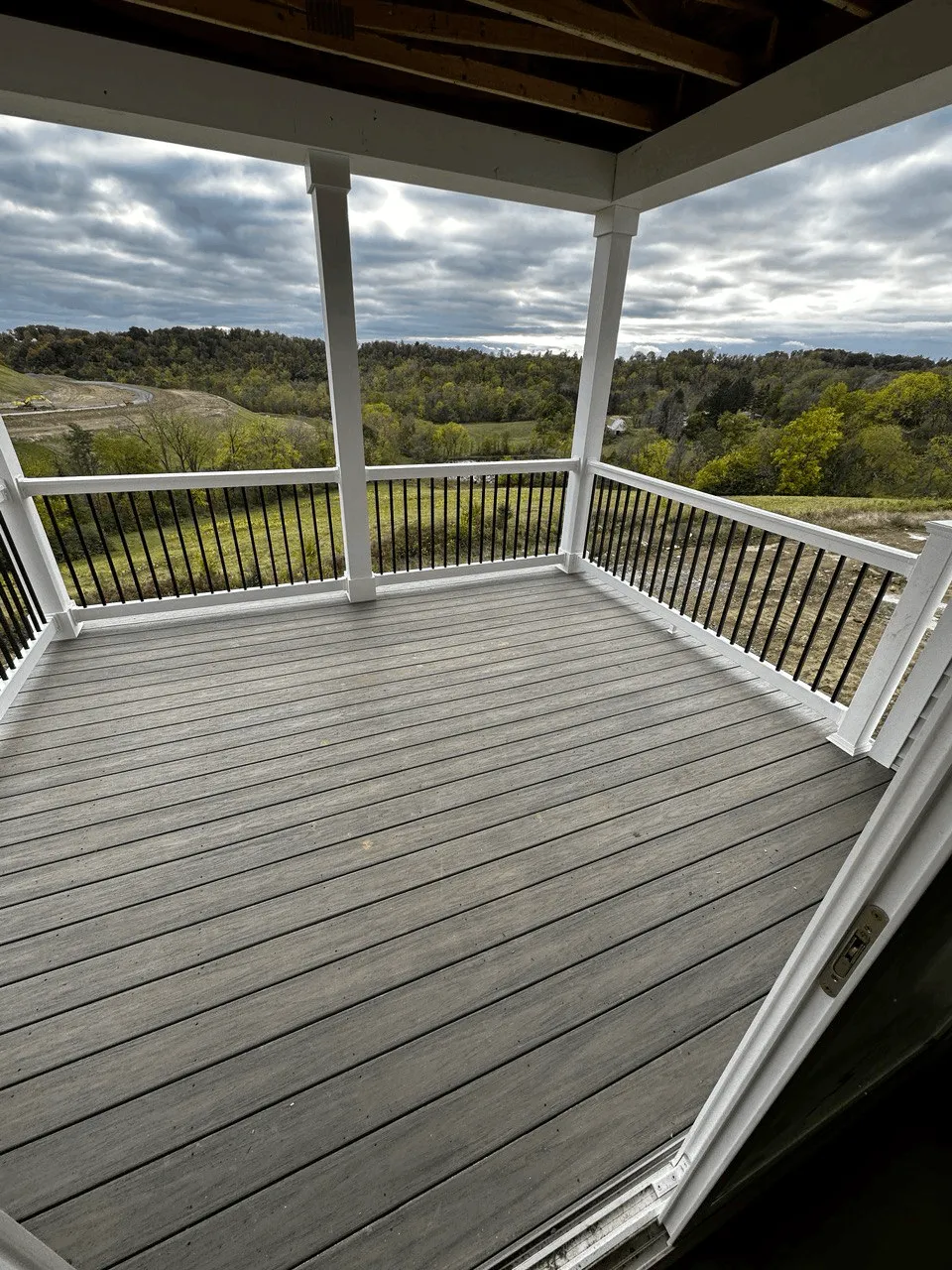 Covered deck with light gray decking and white posts overlooking a wooded valley