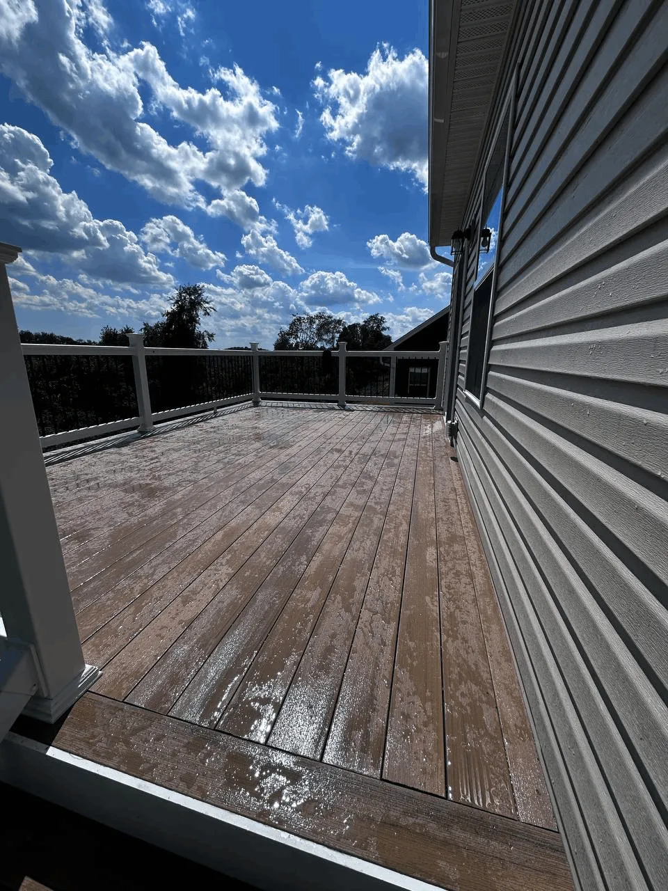 Brown composite deck boards after rain alongside gray siding and white railings