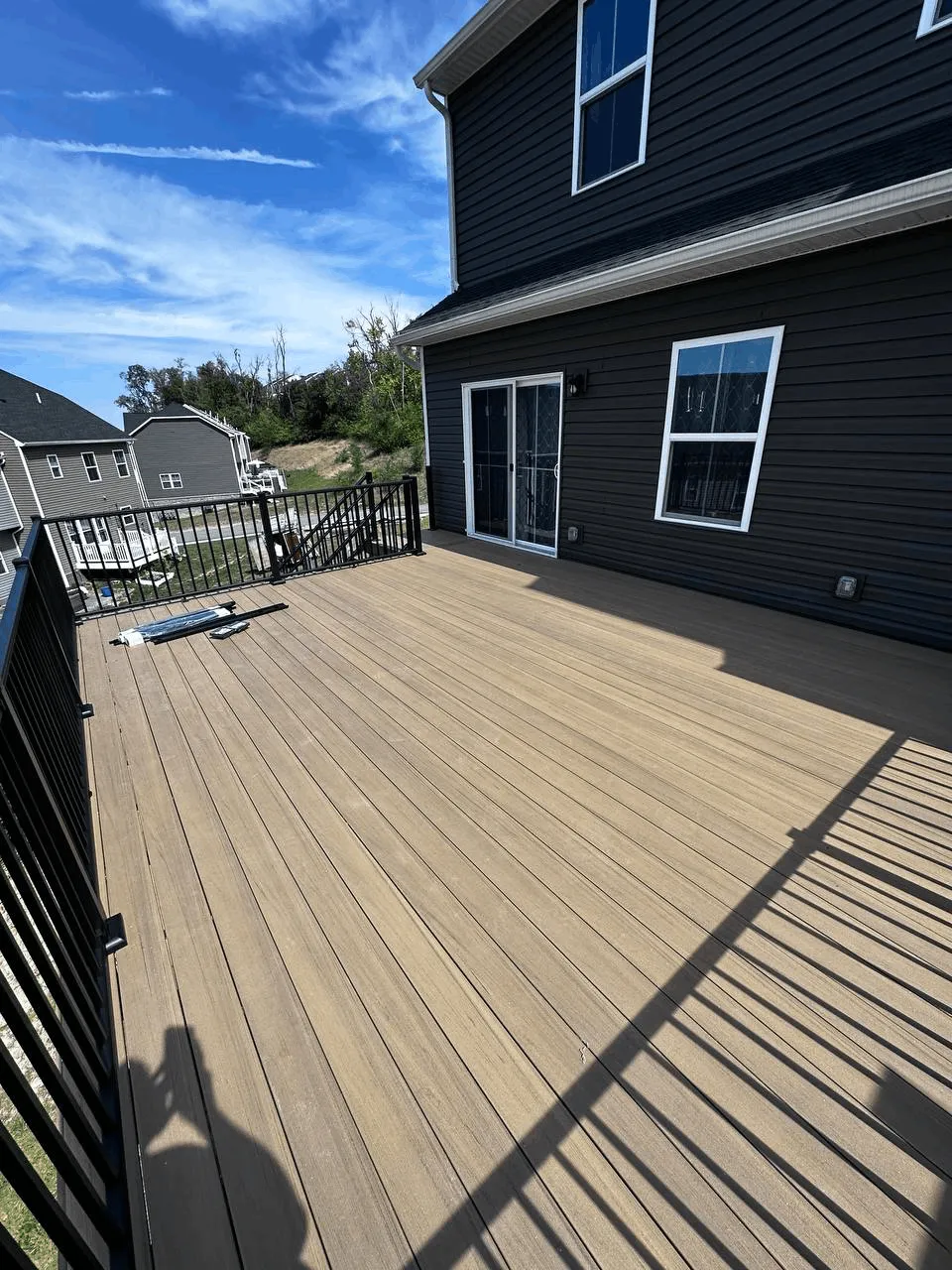 Large tan composite deck with black aluminum railings against dark navy siding