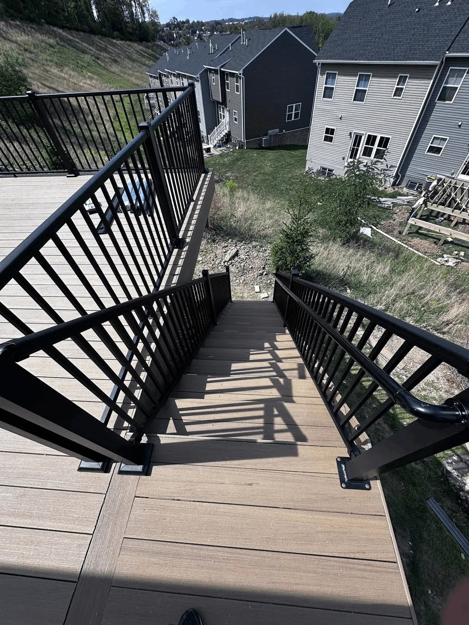 Black aluminum railing sections installed along a tan composite deck on a hillside lot