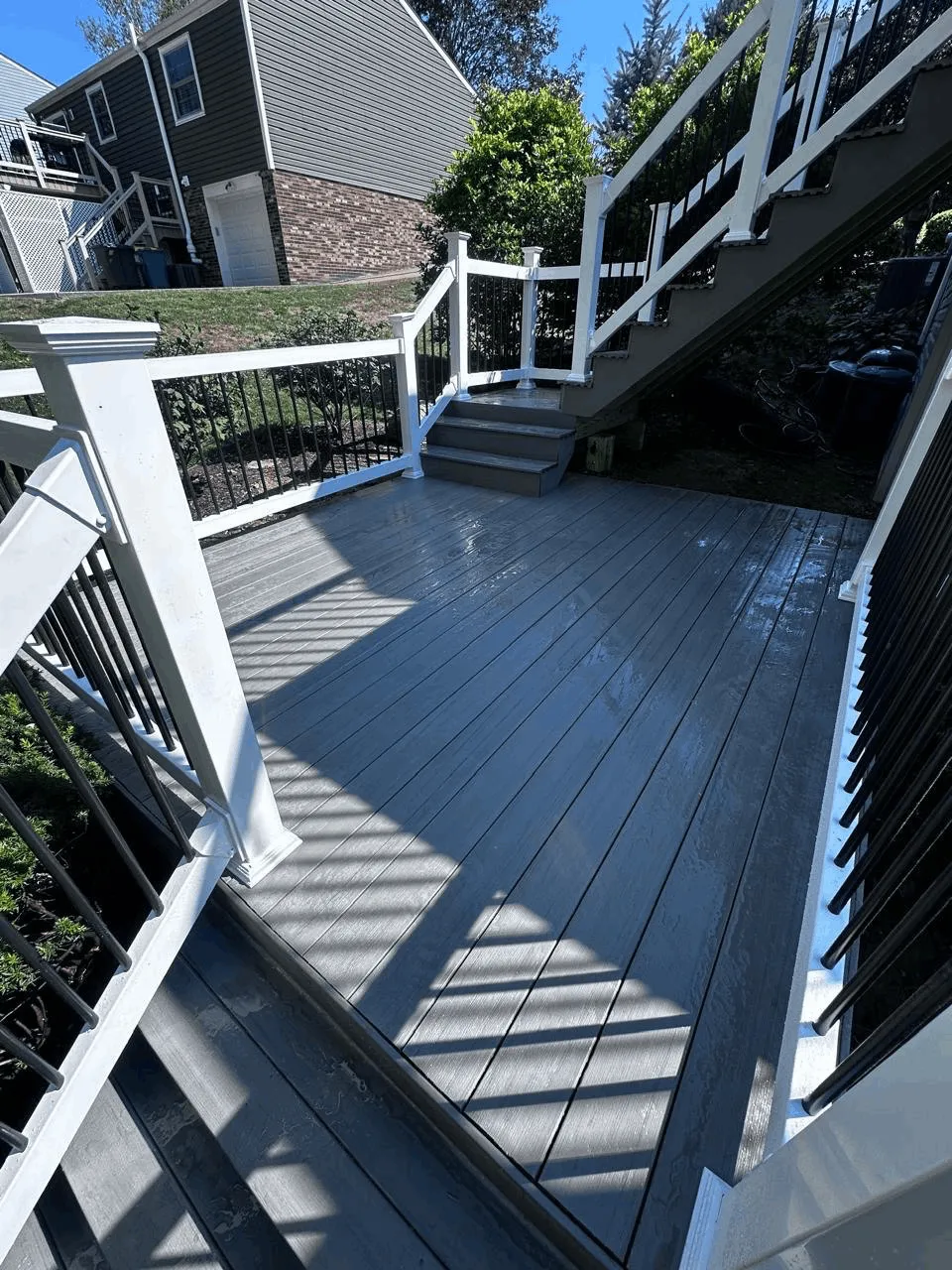 Gray composite deck with white railings, black balusters, and stairs to an upper landing