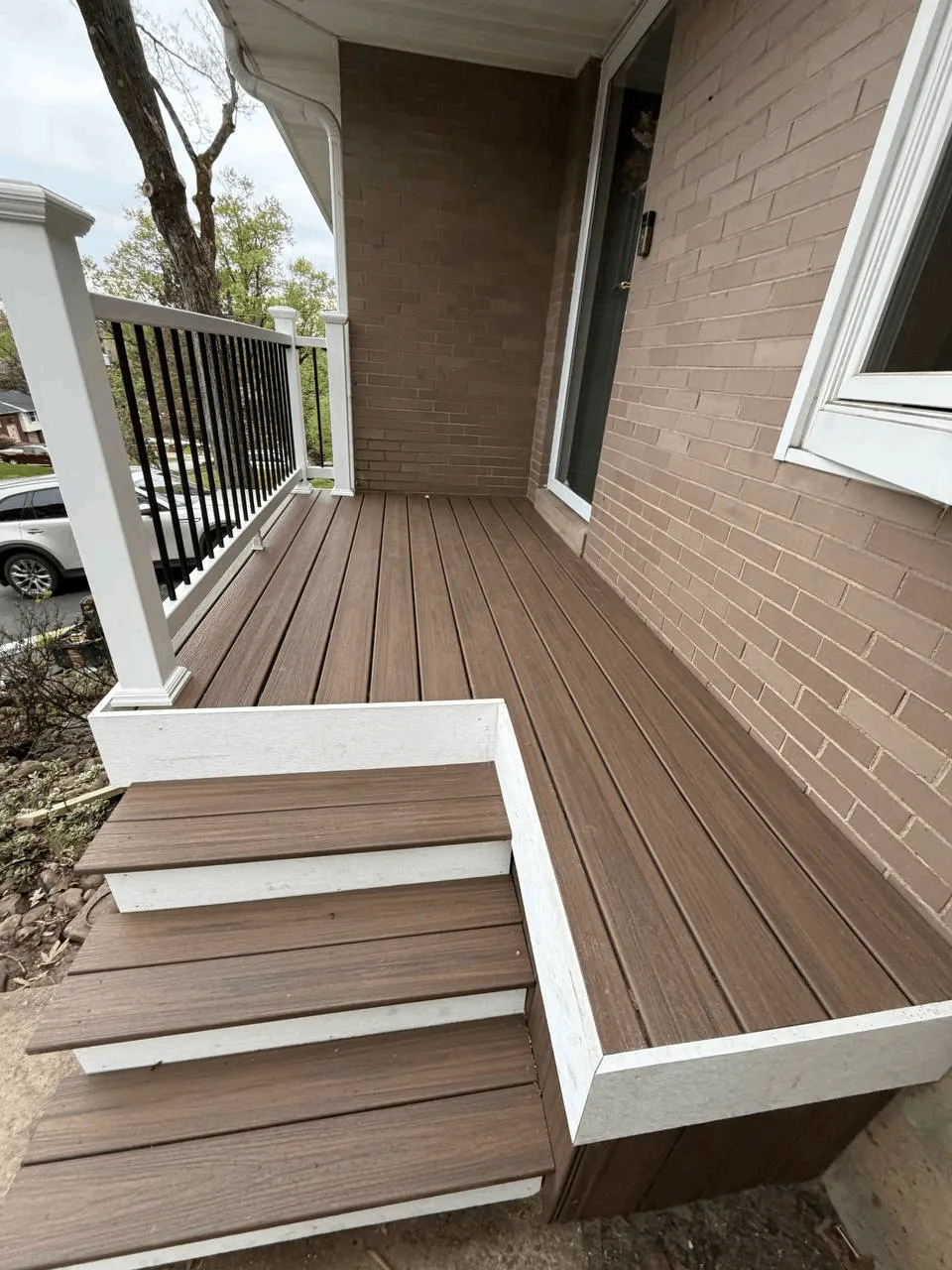 Brown composite deck with white fascia trim and black railings on a brick home