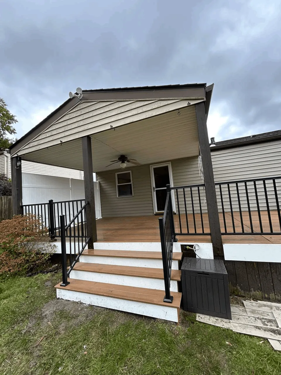 Covered front porch with a ceiling fan, black railings, and wide wooden entry steps