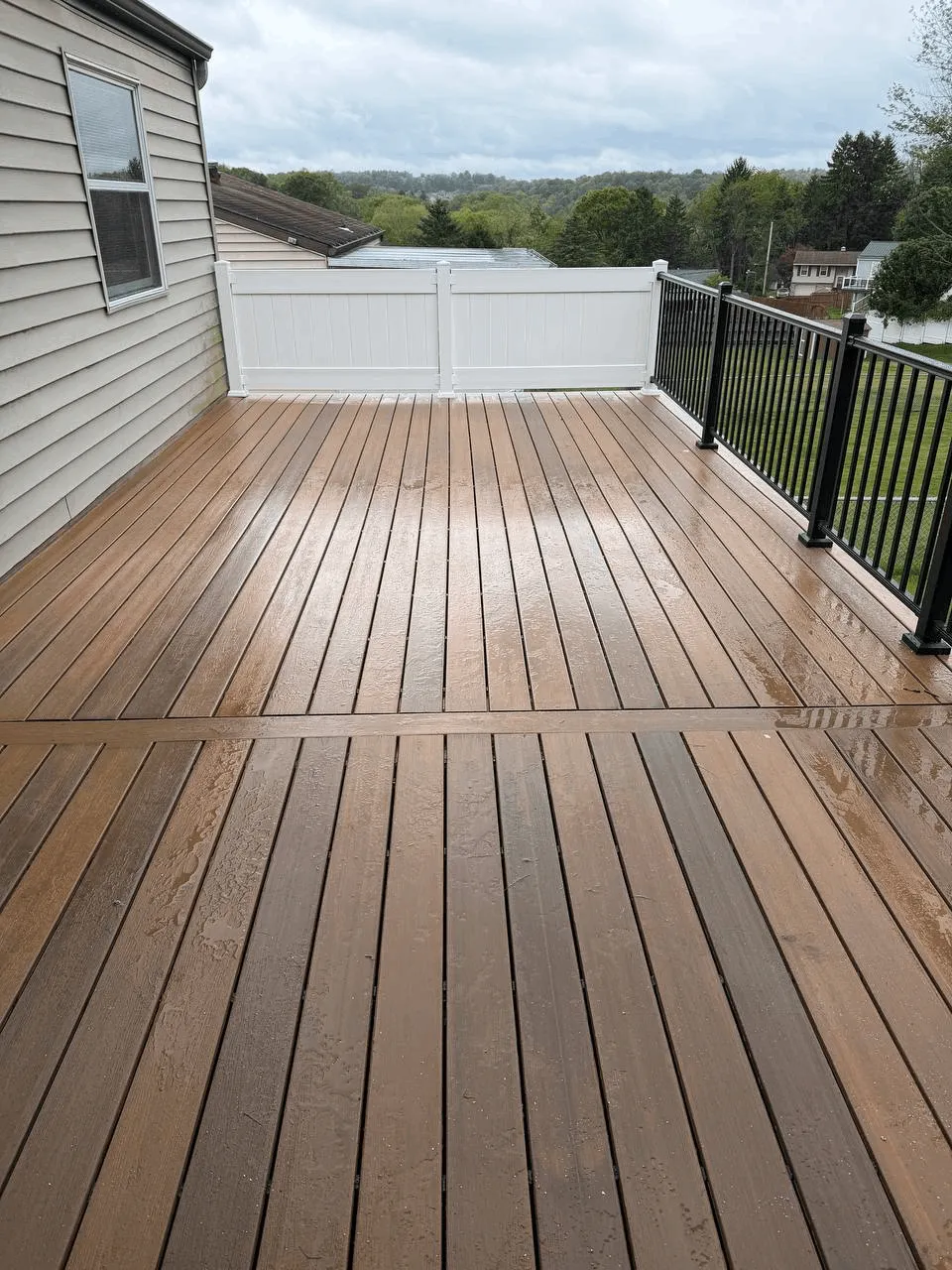 Brown composite deck with black aluminum railings and a white privacy fence panel