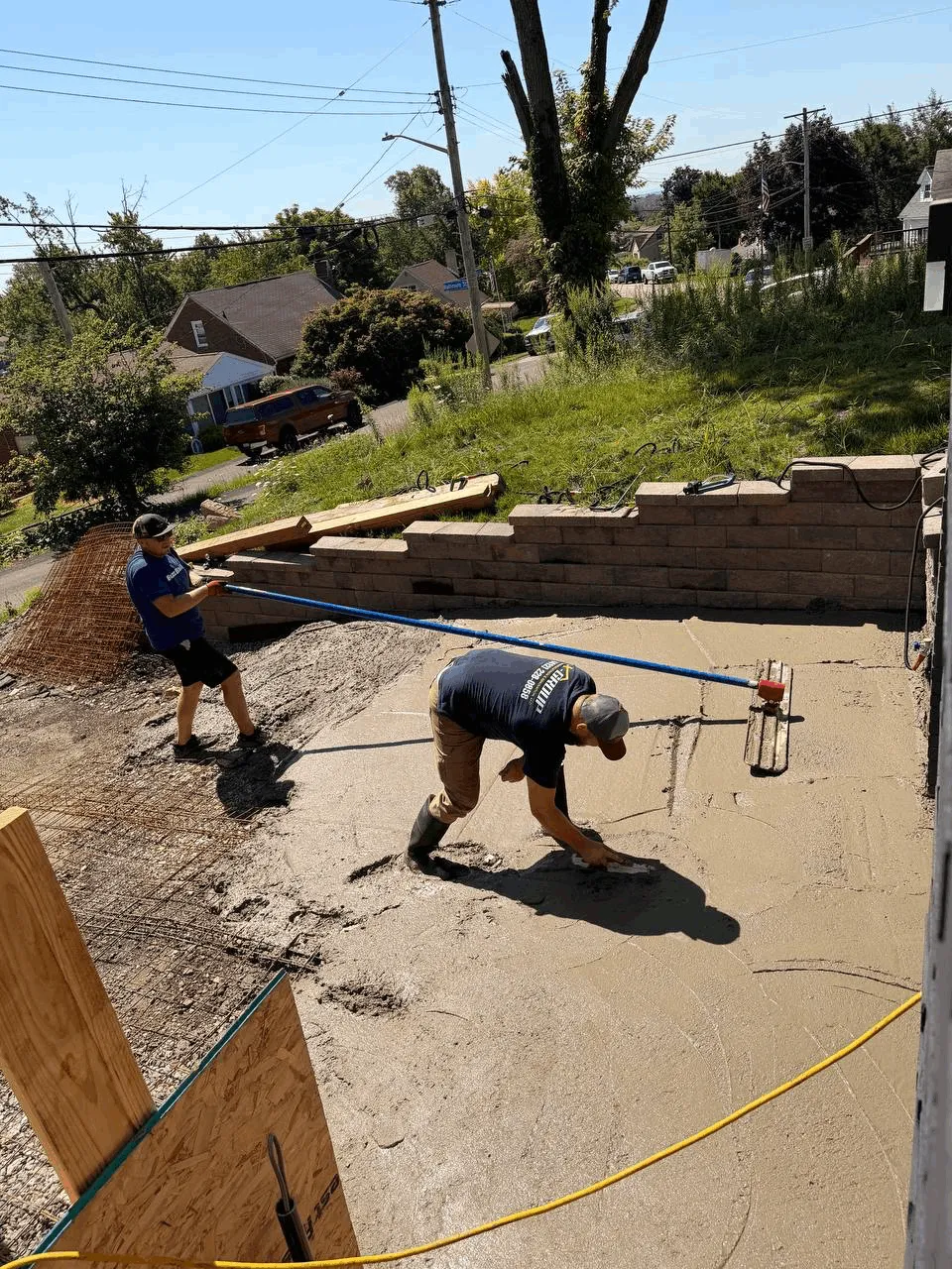 Two crew members pulling a screed across a freshly poured concrete slab