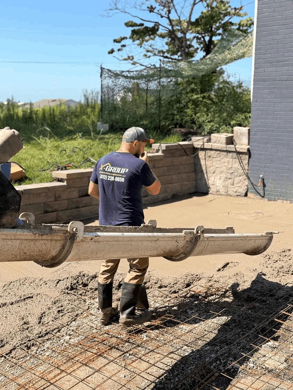 X-Group crew member screeding fresh concrete beside a block retaining wall