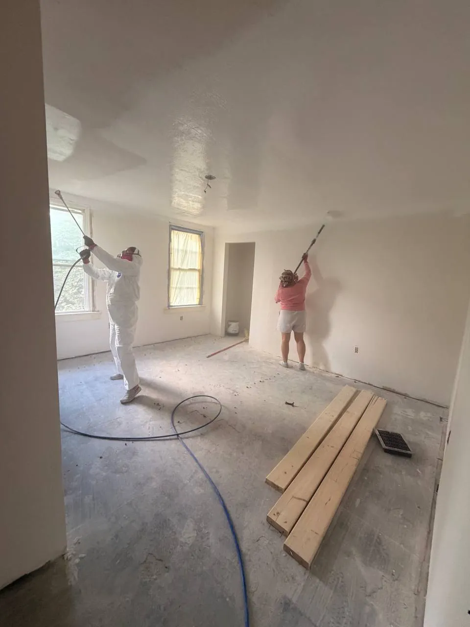 Crew spraying and finishing walls and ceiling with flooring stacked on the floor