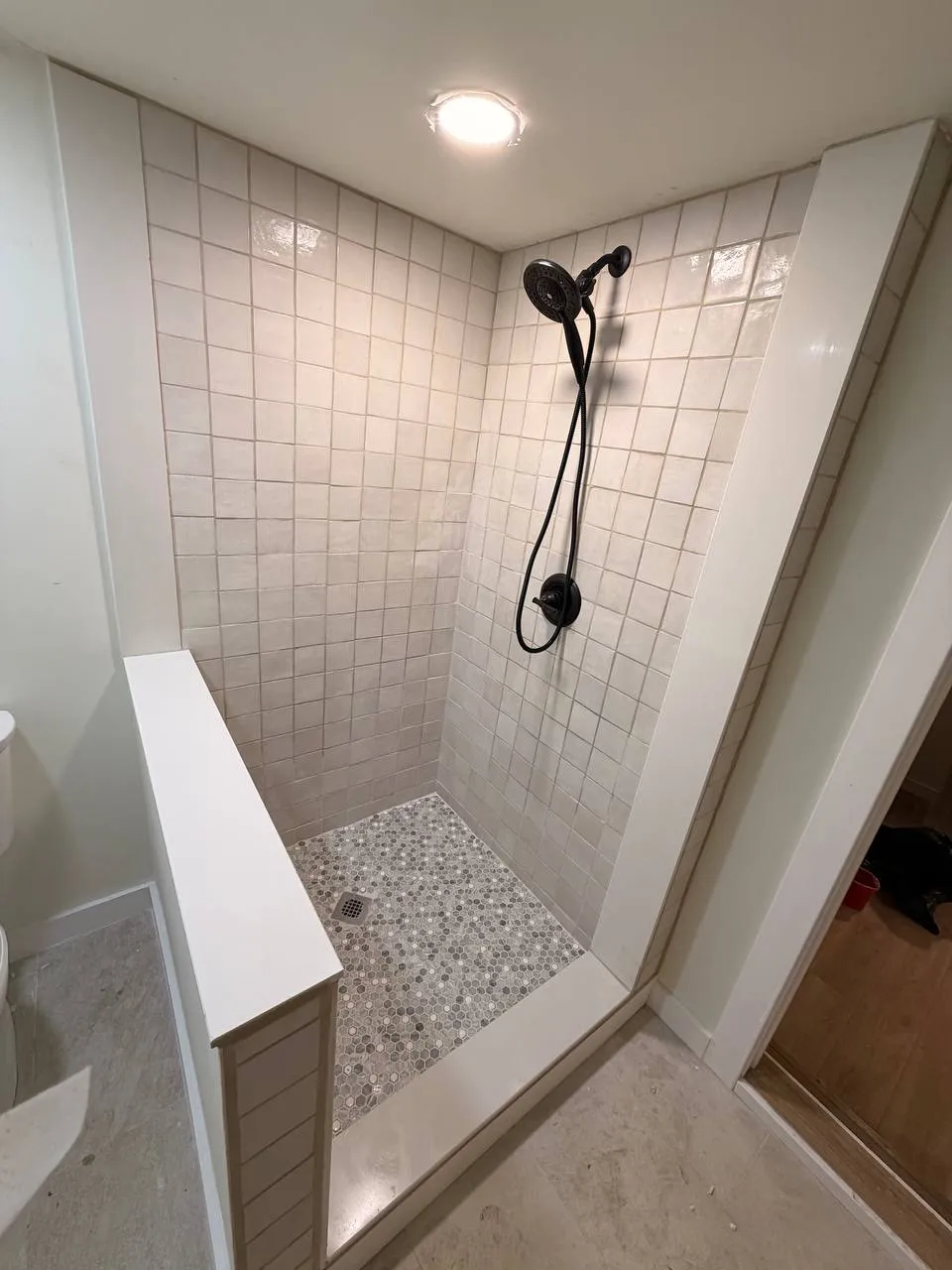 Finished walk-in shower with white square tile, black fixtures, and a pebble floor