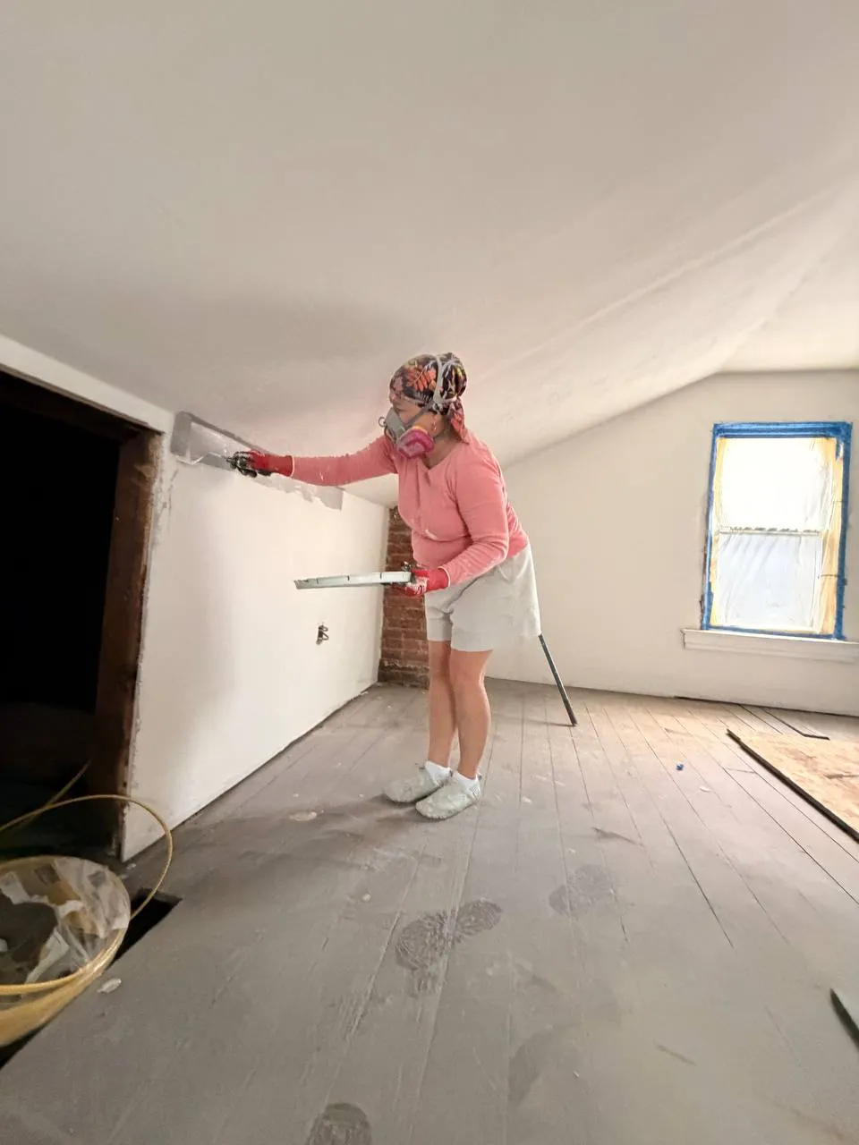 Crew member skim coating a wall in a sloped ceiling attic room