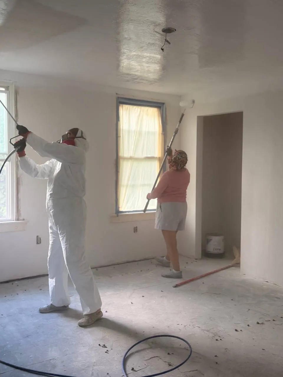 Two crew members spraying wall and ceiling finish in an empty room
