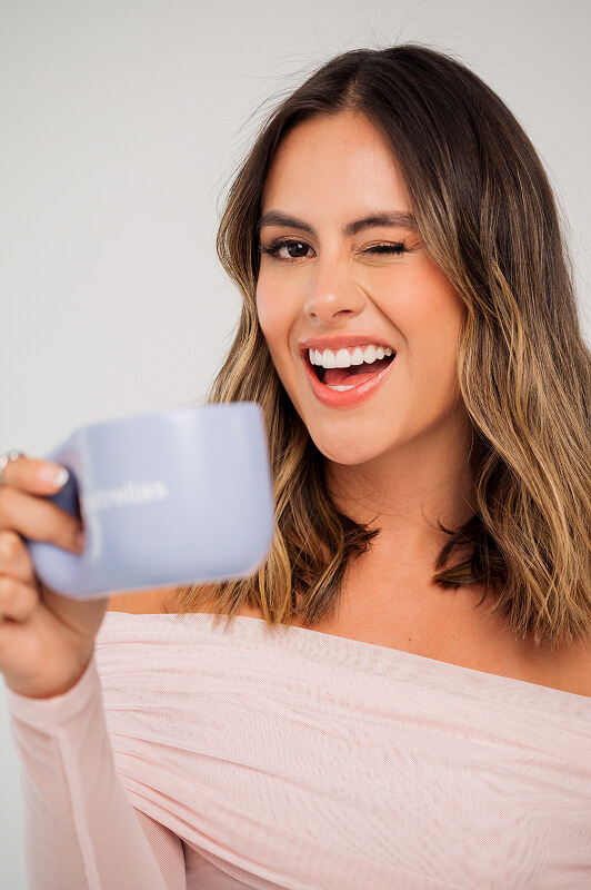 Mujer sonriente guiñando un ojo mientras sostiene una taza de estrellas app