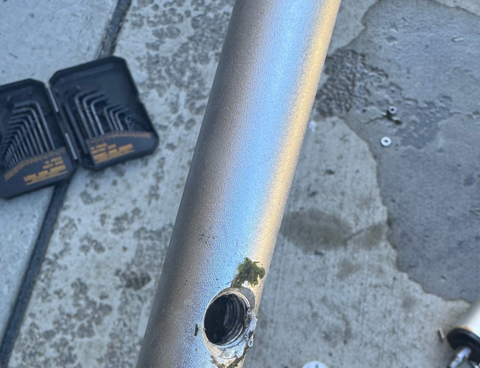 Close up of a hole worn through the metal handle tube of the surface cleaner, next to a set of hex keys