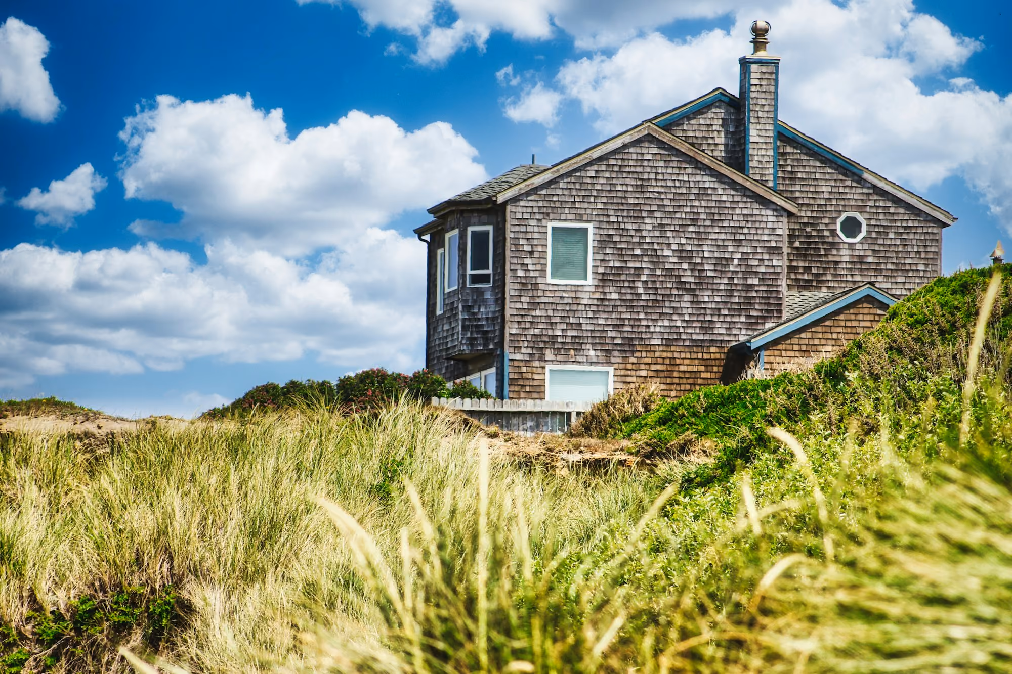 A shingled coastal house standing exposed above the dune grass
