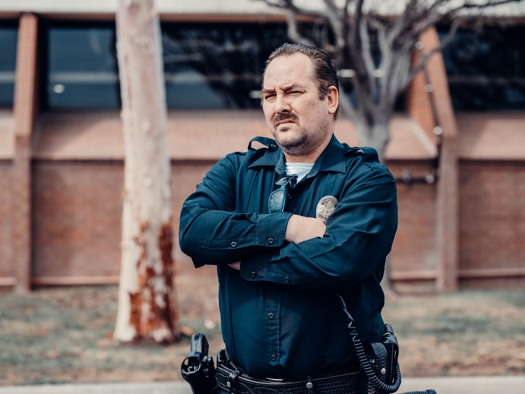 A determined police officer standing with arms crossed outside a building, showcasing authority.