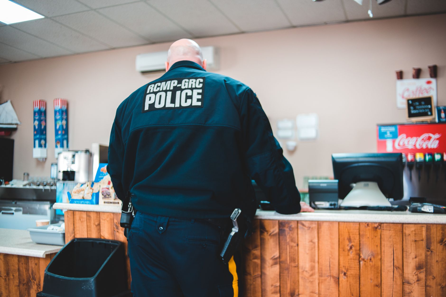 A police officer standing at a café counter ordering coffee, back view.