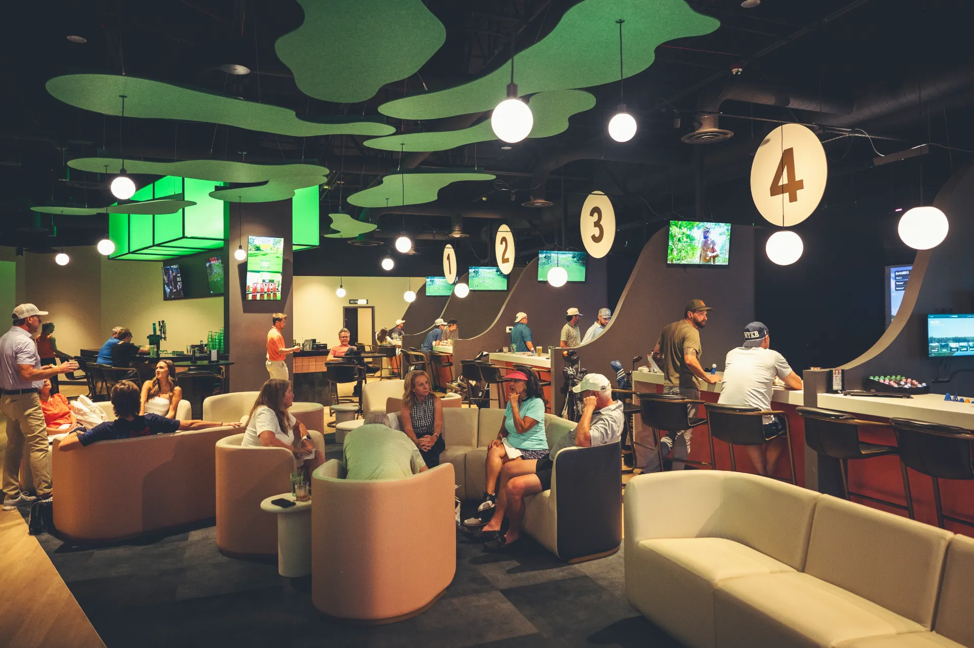 Guests relaxing on lounge sofas near golf simulator bays at The PAR Club
