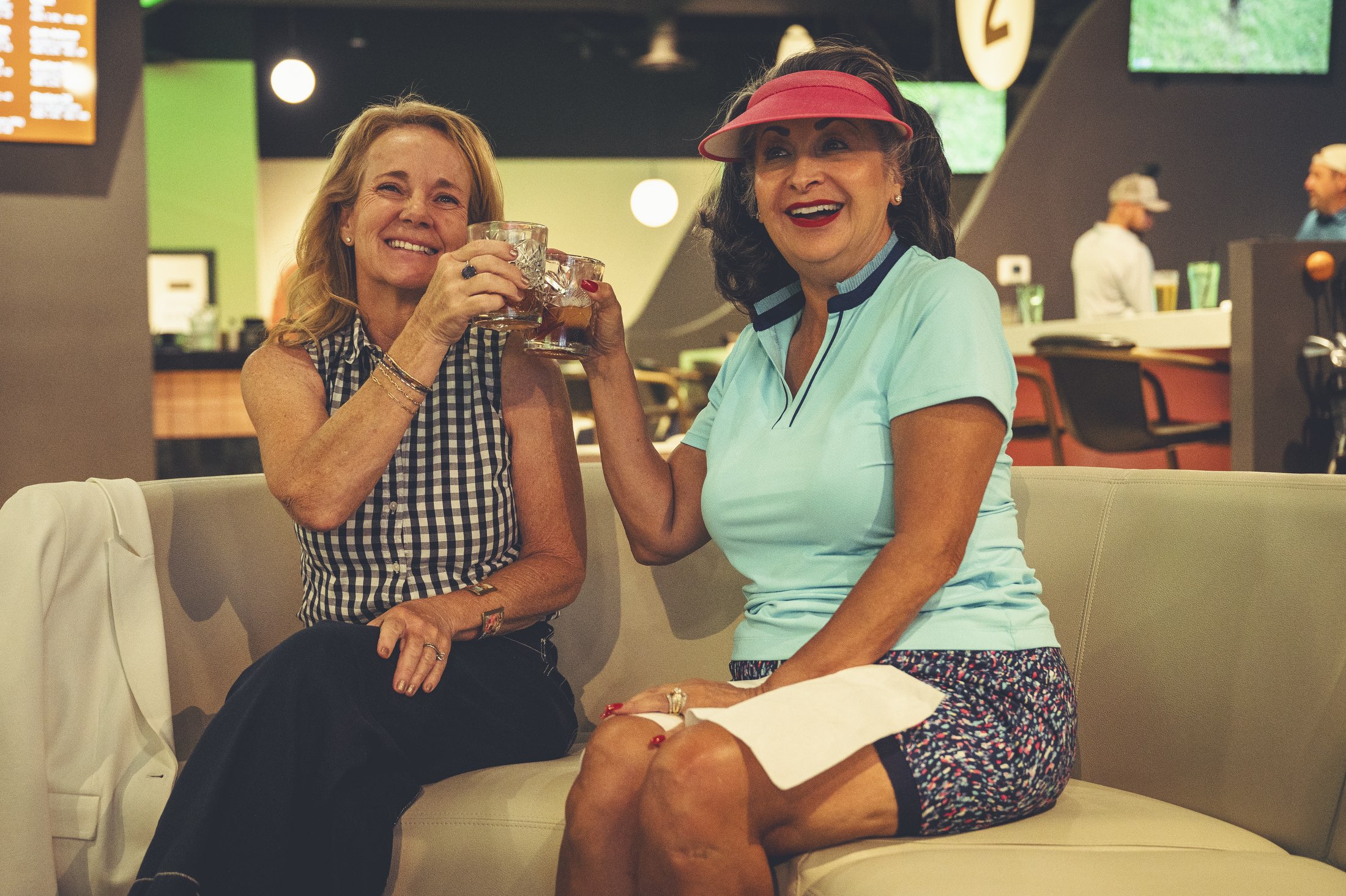 Two women toasting drinks on lounge seating at The PAR Club