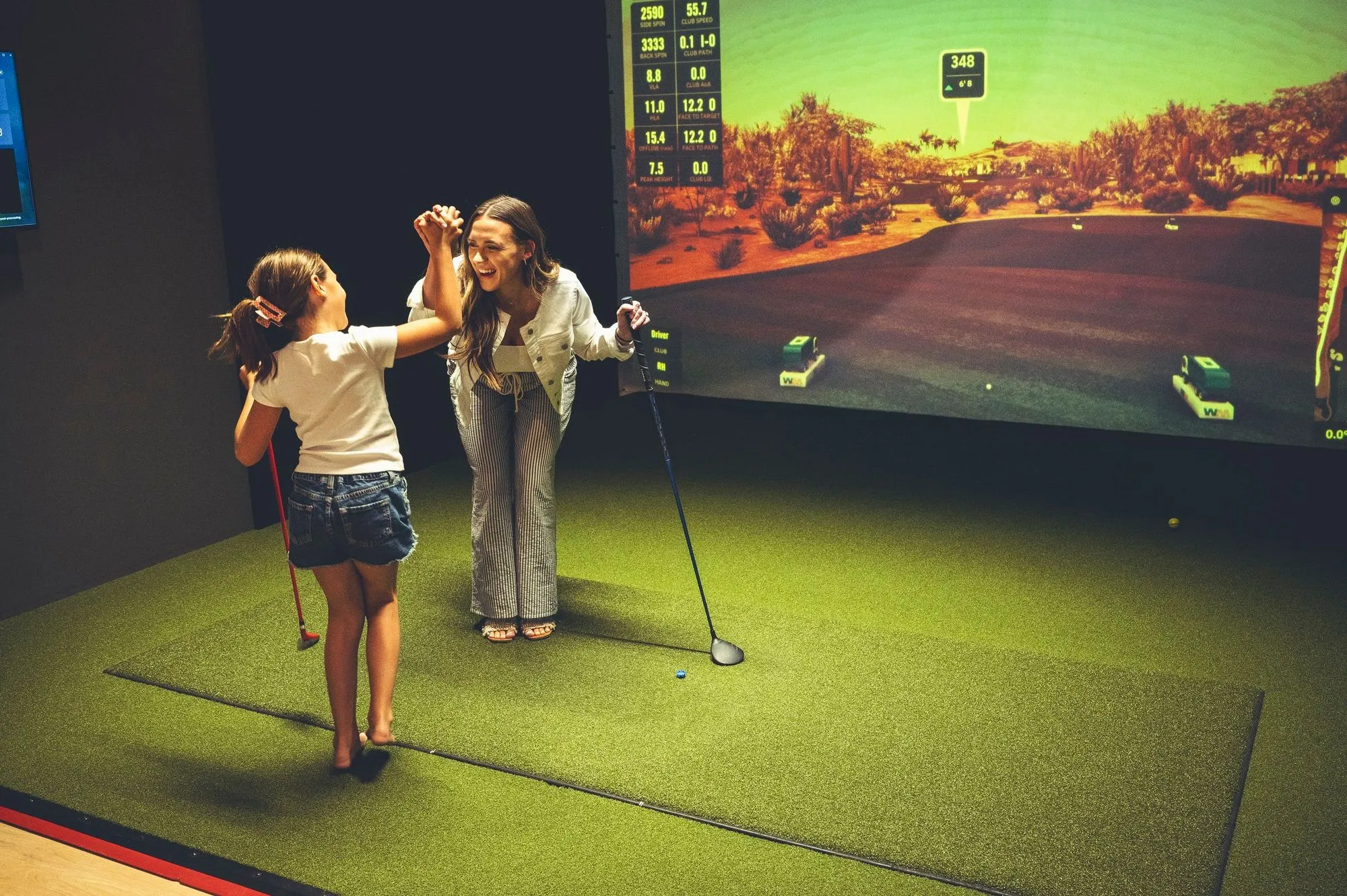Mother and daughter high-fiving after a swing on the golf simulator at The PAR Club 