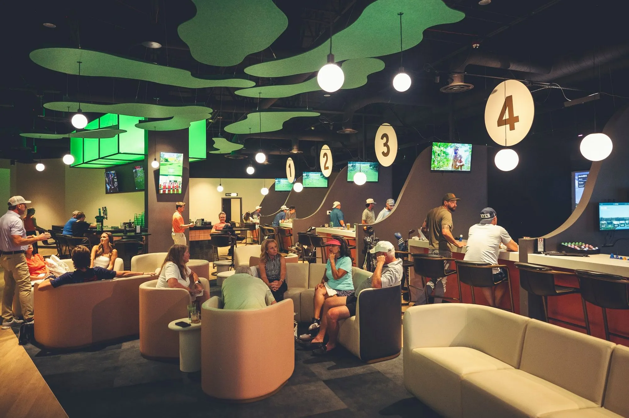 Guests relaxing on lounge sofas near golf simulator bays at The PAR Club
