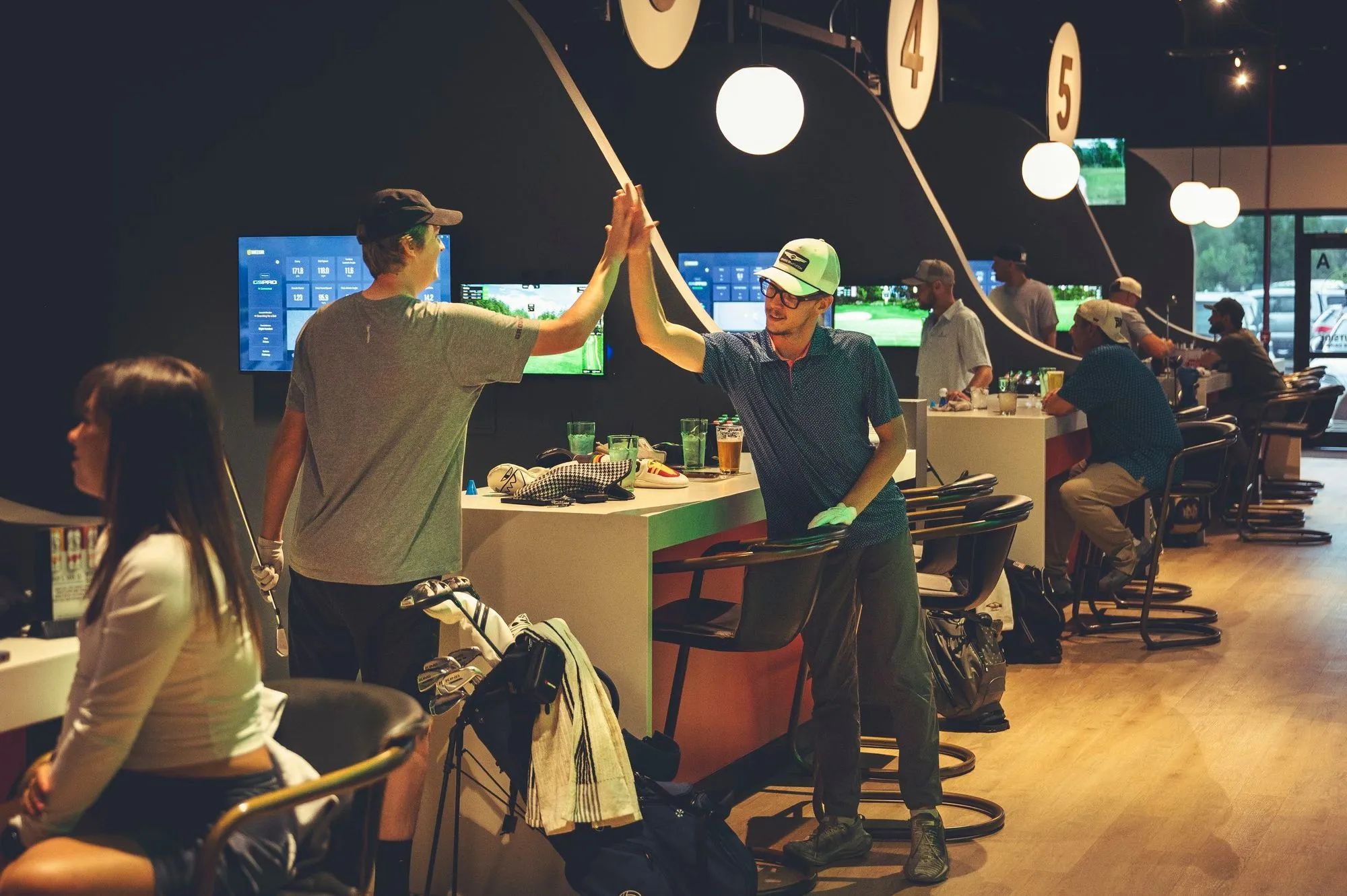 Friends high-fiving between golf simulator bays at The PAR Club