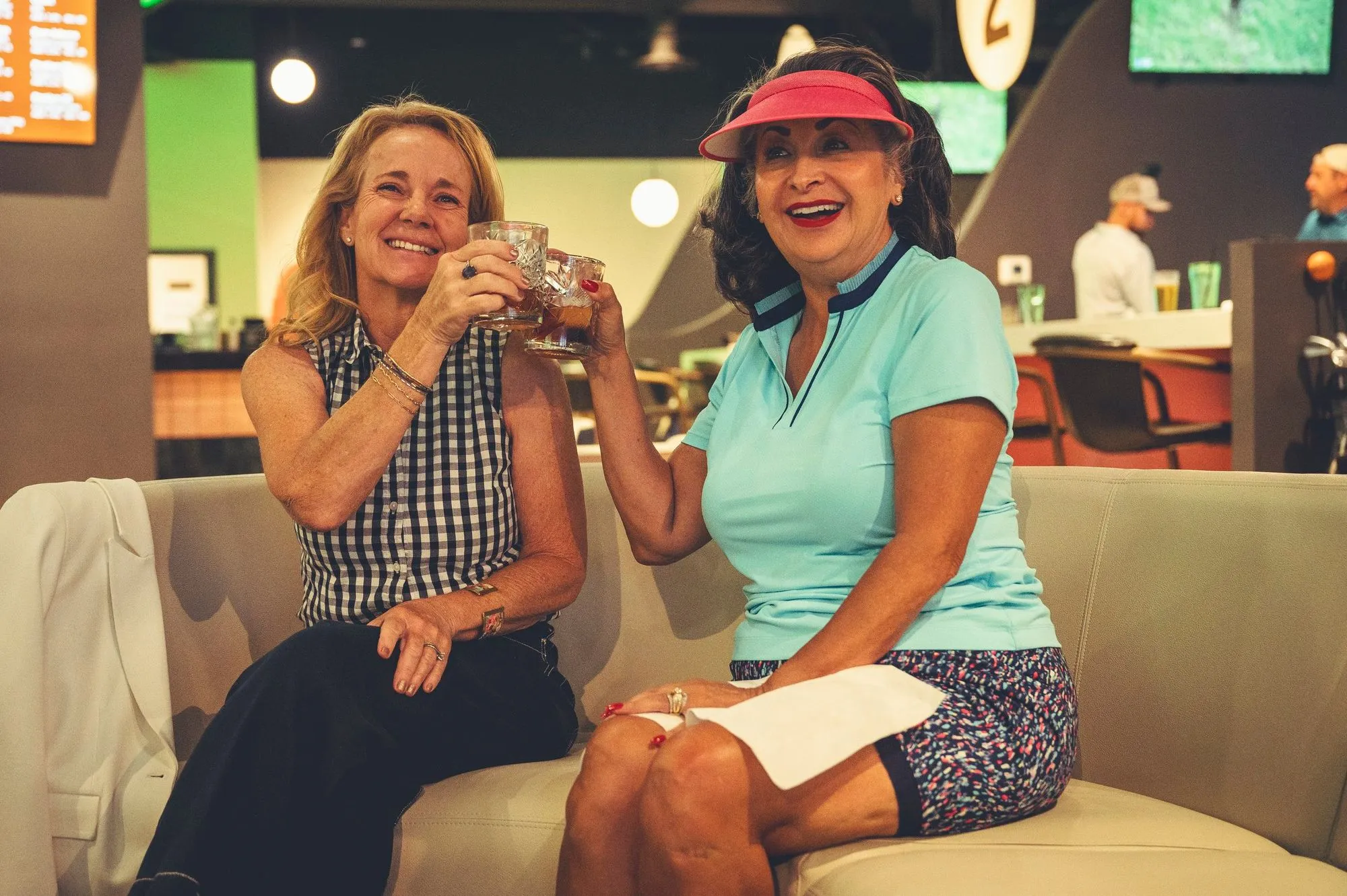 Two women toasting drinks on lounge seating at The PAR Club
