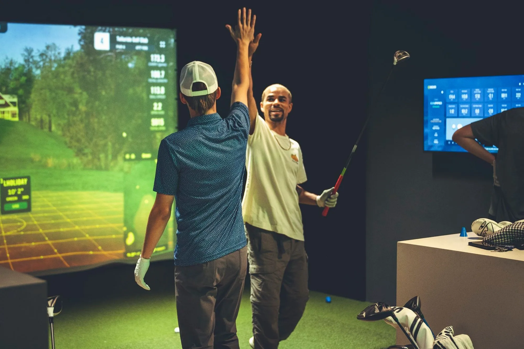Friends high-fiving after a great shot on the golf simulator at The PAR Club