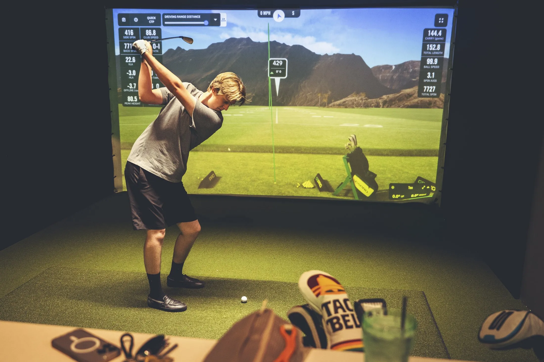 Guest taking a swing on the golf simulator at The PAR Club with shot data displayed